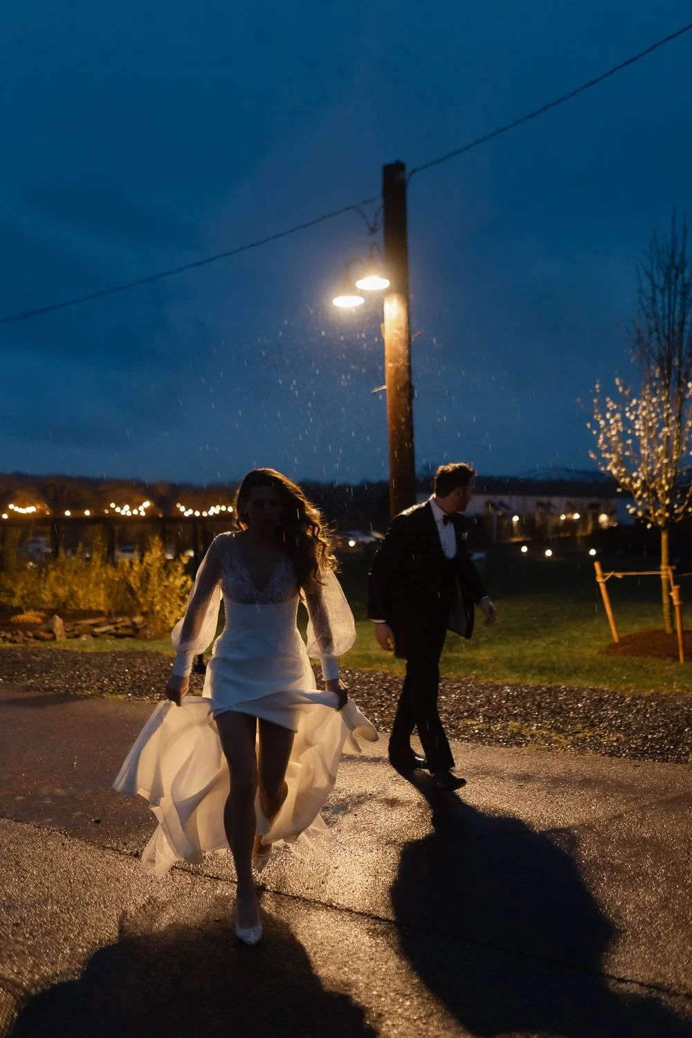Couple captured at night with blue sky and rain drops silhouetting them under a street light.
