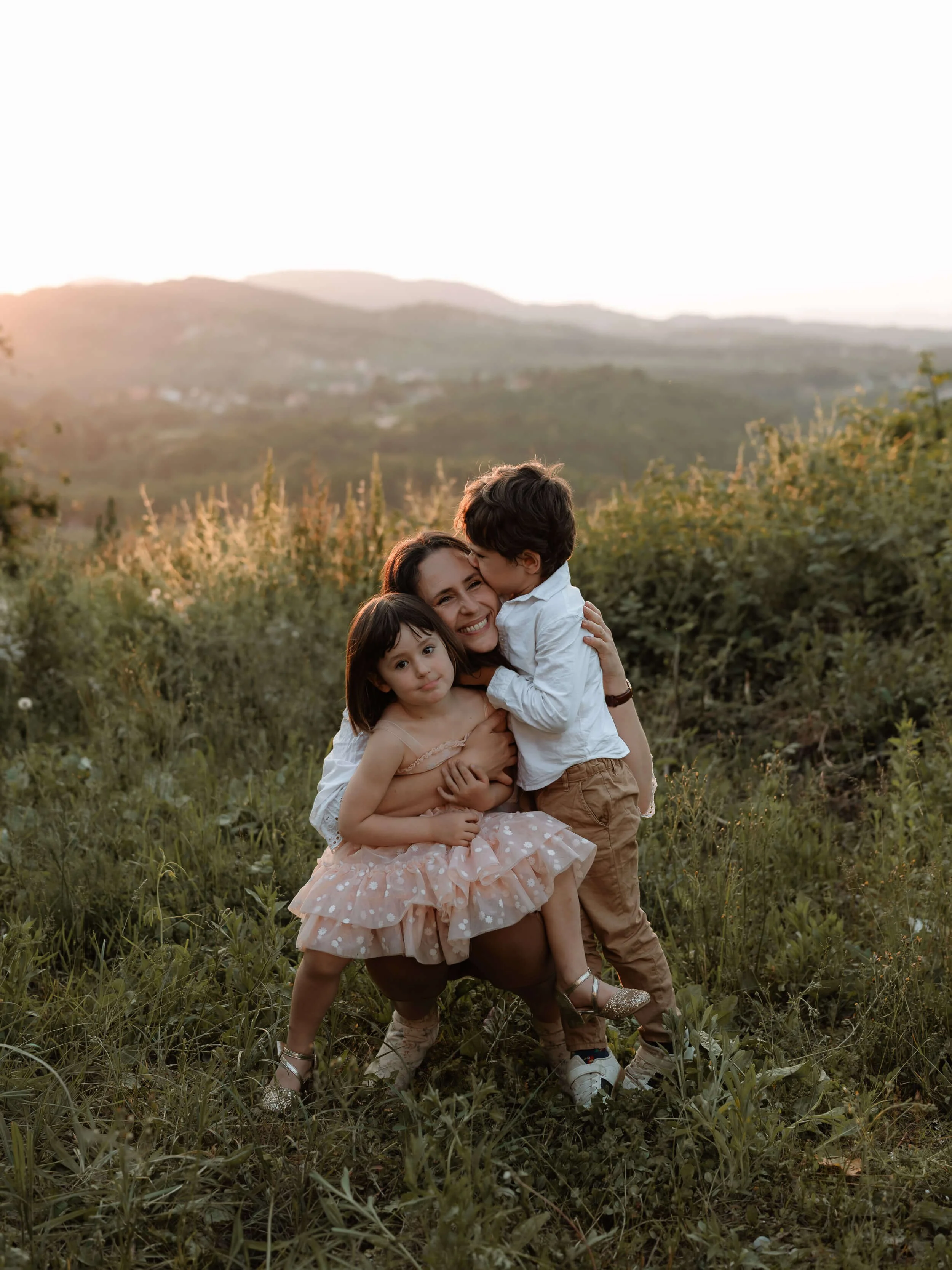 Mama grli dvoje male djece tijekom fotografiranja u prirodi