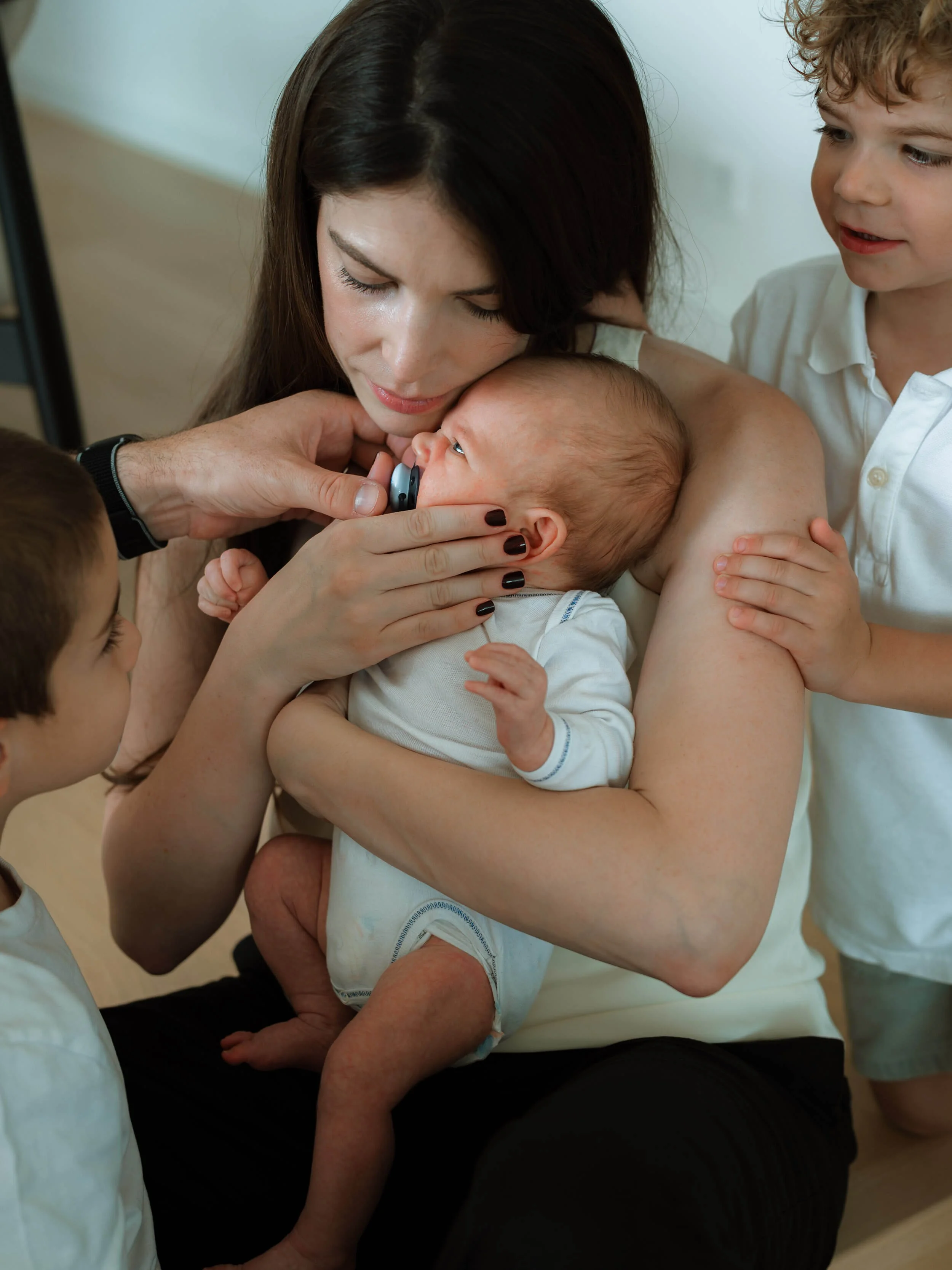 Mama drži bebu u naručju okružena sa svoja dva sina