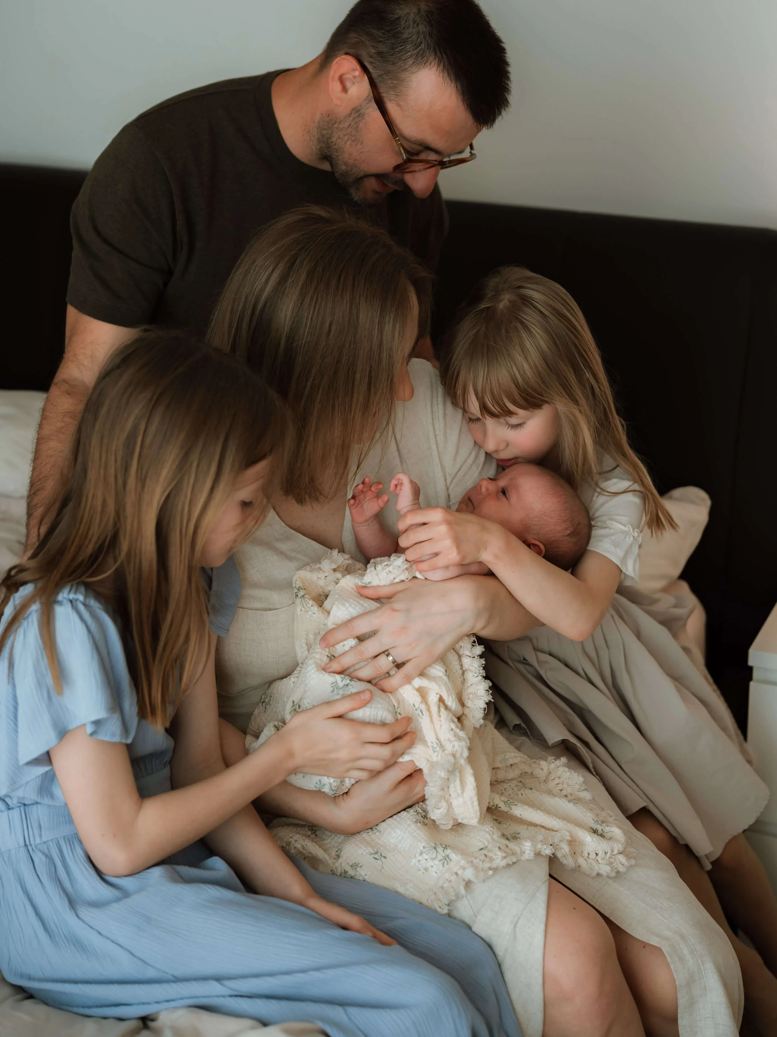 Family gathered on a bed, celebrating the arrival of a newborn baby.