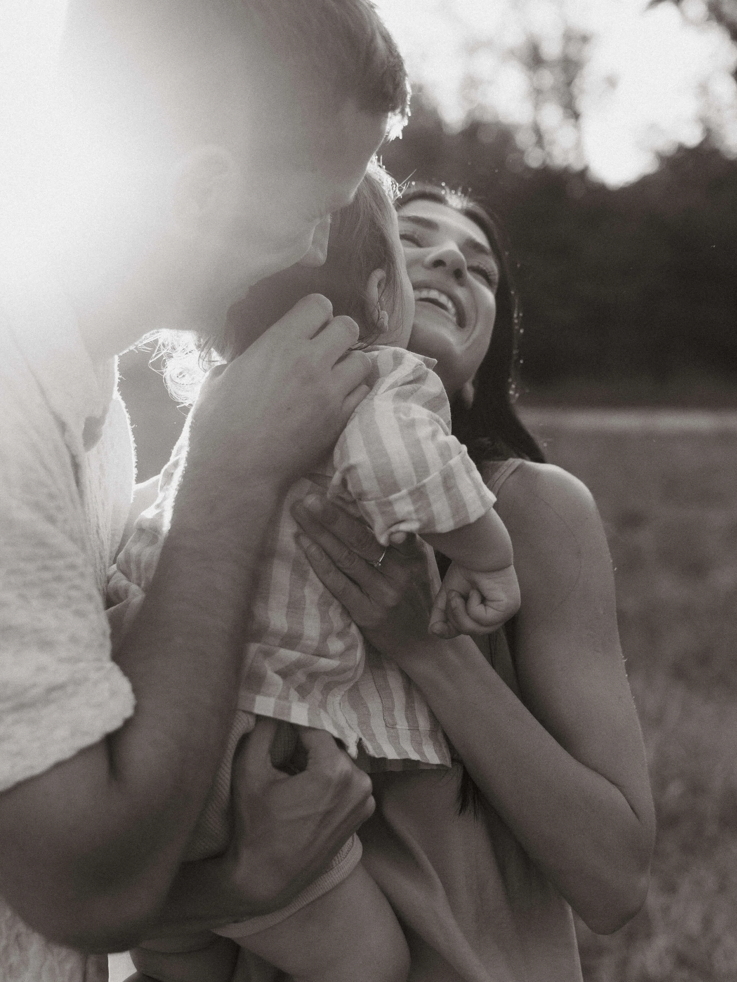 A woman, a man, and a young girl are enjoying a moment together outdoors, smiling and laughing in sunlight.