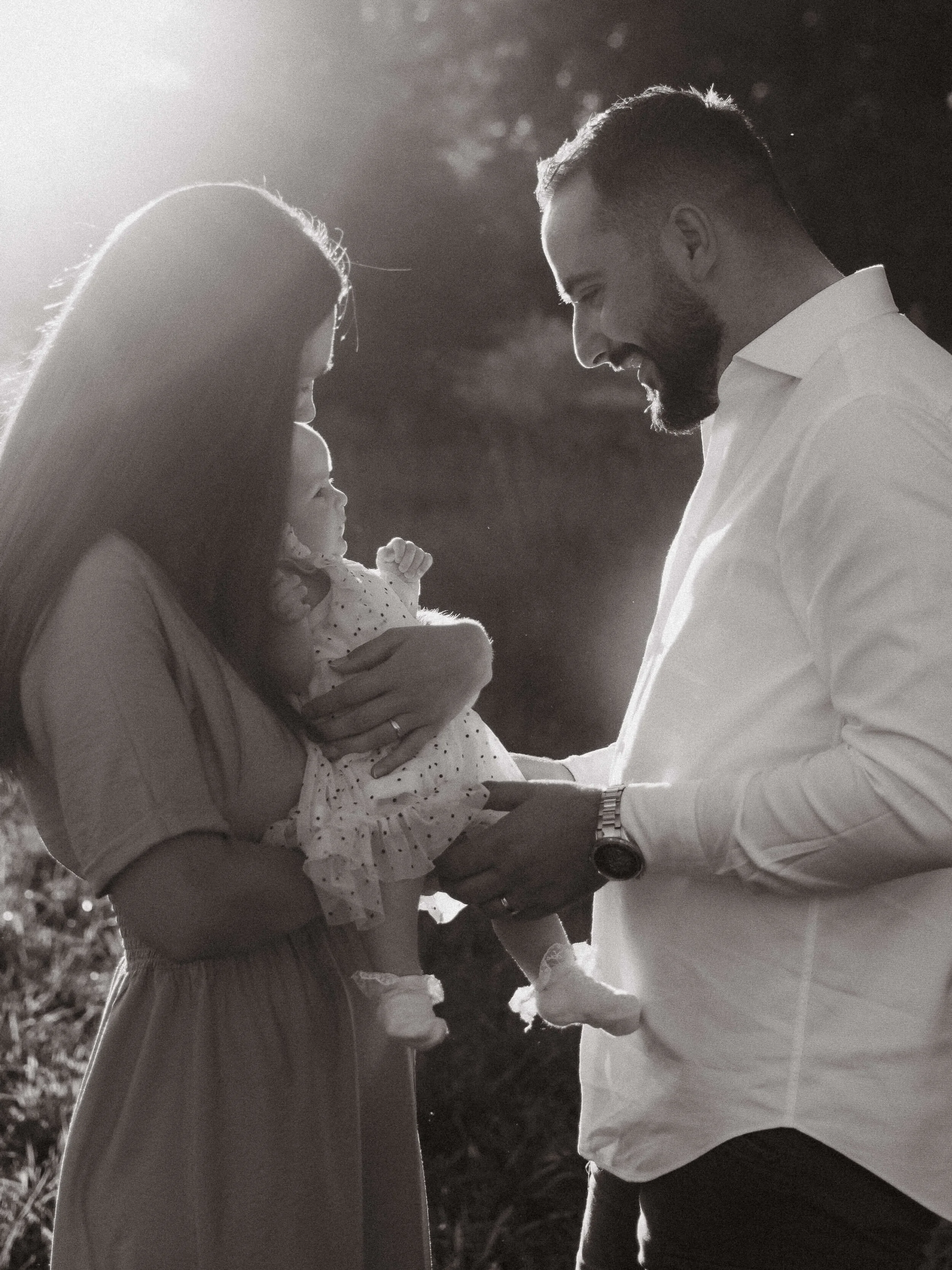Crno-bijela fotografija roditelja u igri sa svojom bebom u zalazak sunca