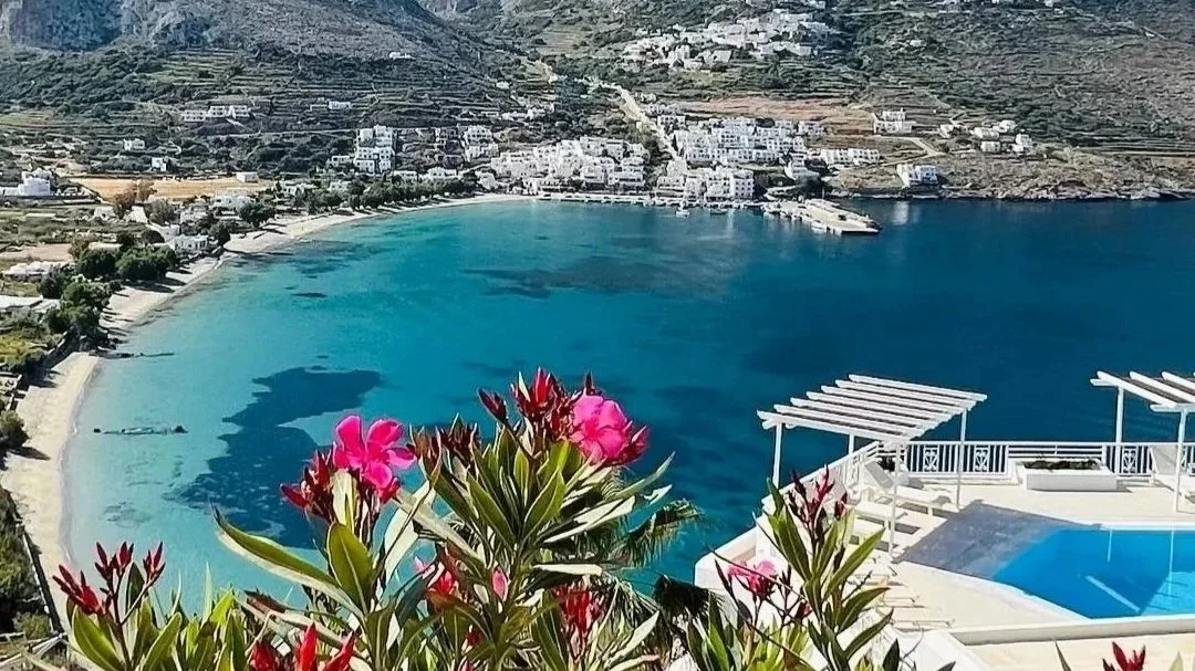 Sea view from Aegialis Hotel & Spa in Amorgos, Greece, overlooking Aegiali Bay with mountains, blue water and pink flowers in the foreground.