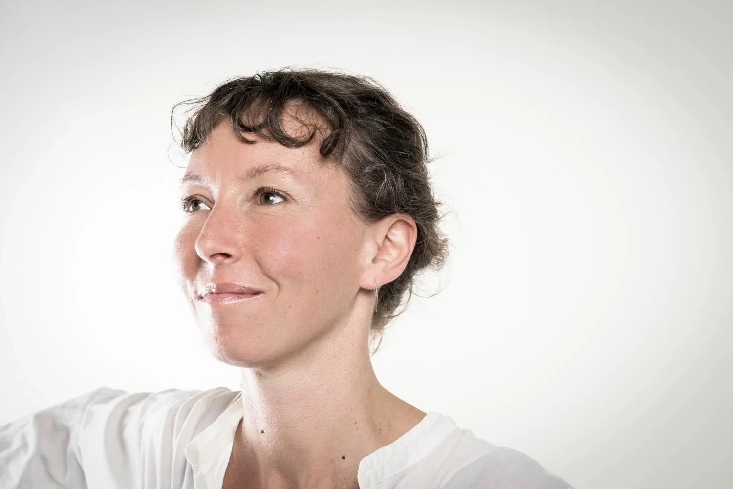 Nahaufnahme einer lachenden Frau mit kurzen braunen Haaren vor hellem Hintergrund.