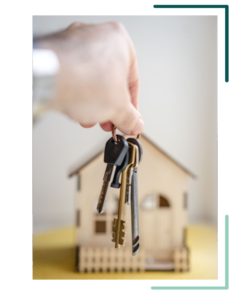 Hand holding keys with a small house model in the background