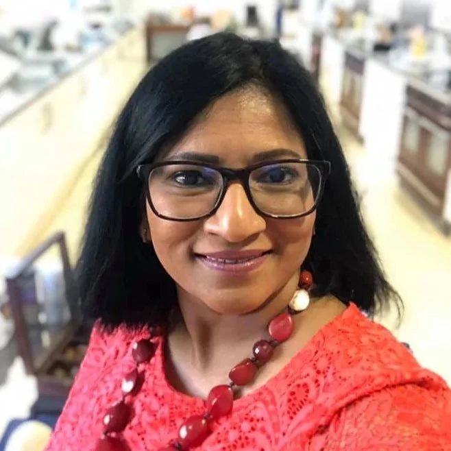 A woman with black hair, glasses, and a red lace top taking a selfie in a kitchen with white appliances and a framed picture on the wall in the background.