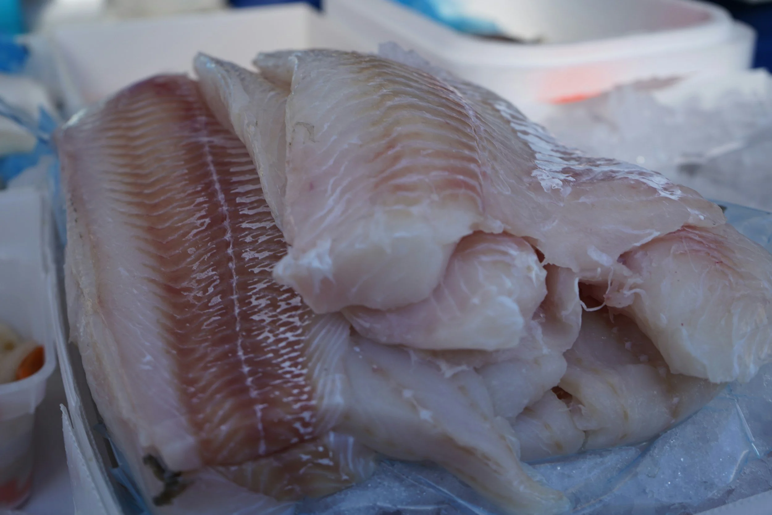 Hand holding a fish on a blue cutting board with a knife nearby.