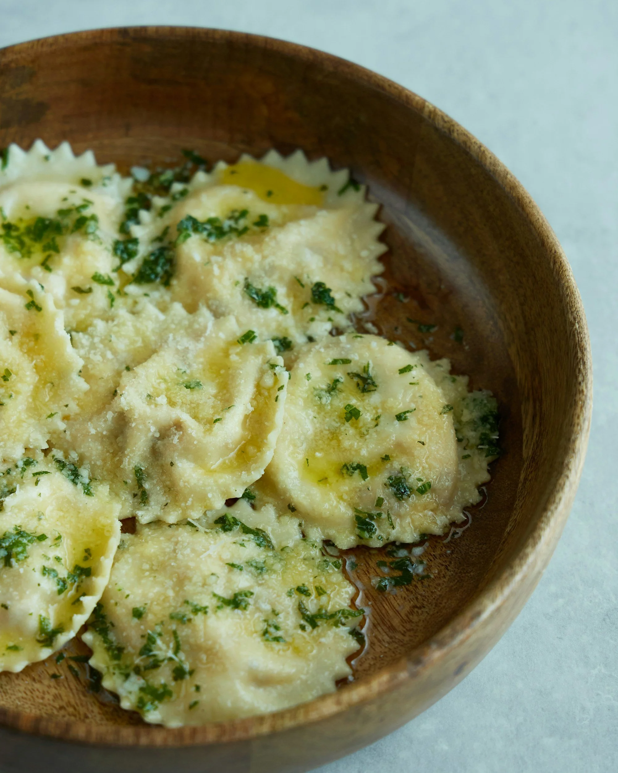 Uncooked ravioli pasta on a floured wooden surface with a ravioli cutter tool to the right.