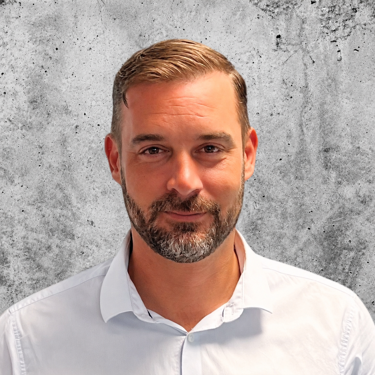 A man with short, slicked-back hair and a beard, wearing a white collared shirt, standing against a blue gradient background.