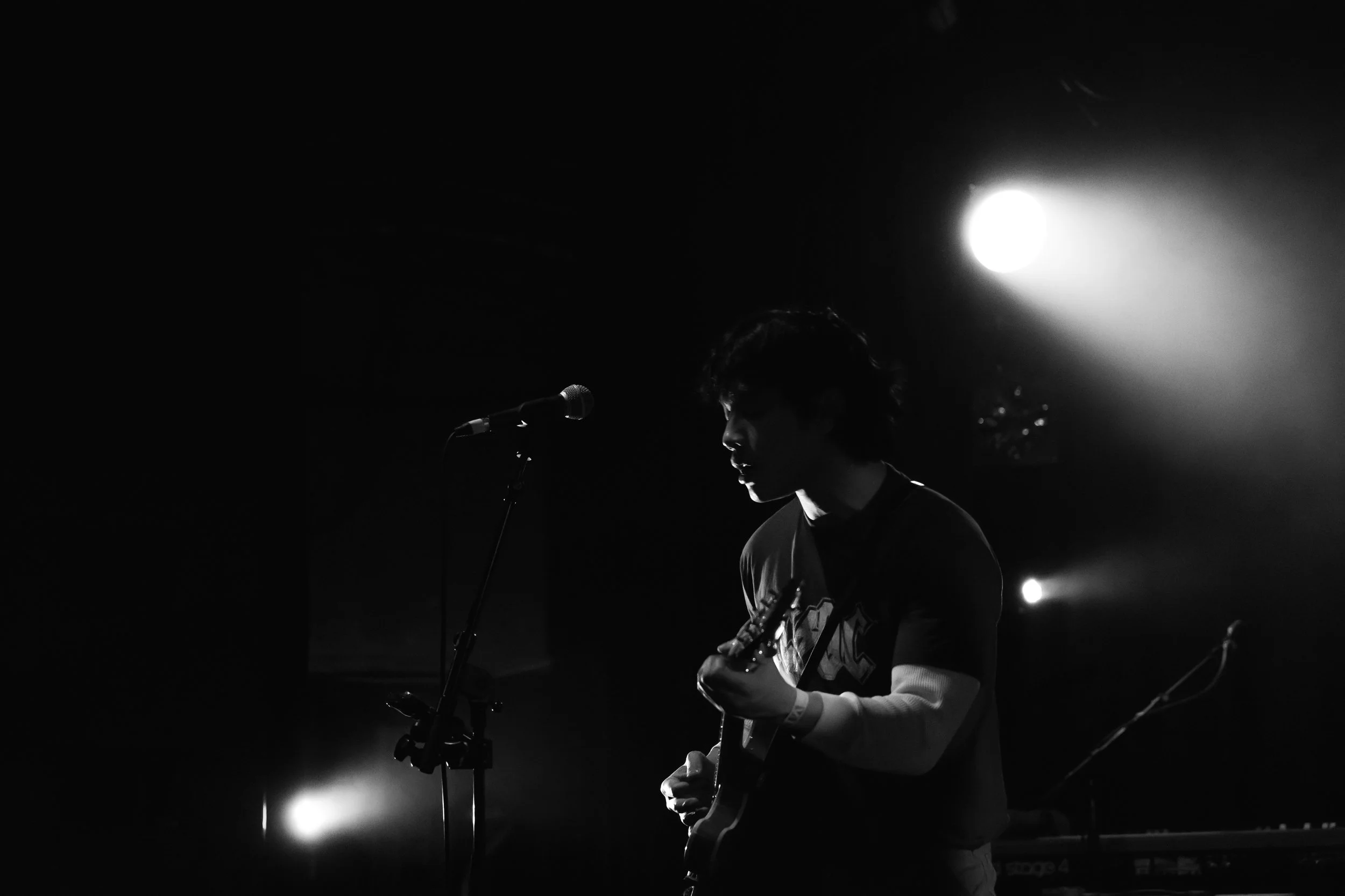 A person playing guitar on stage in darkness with bright stage lights.