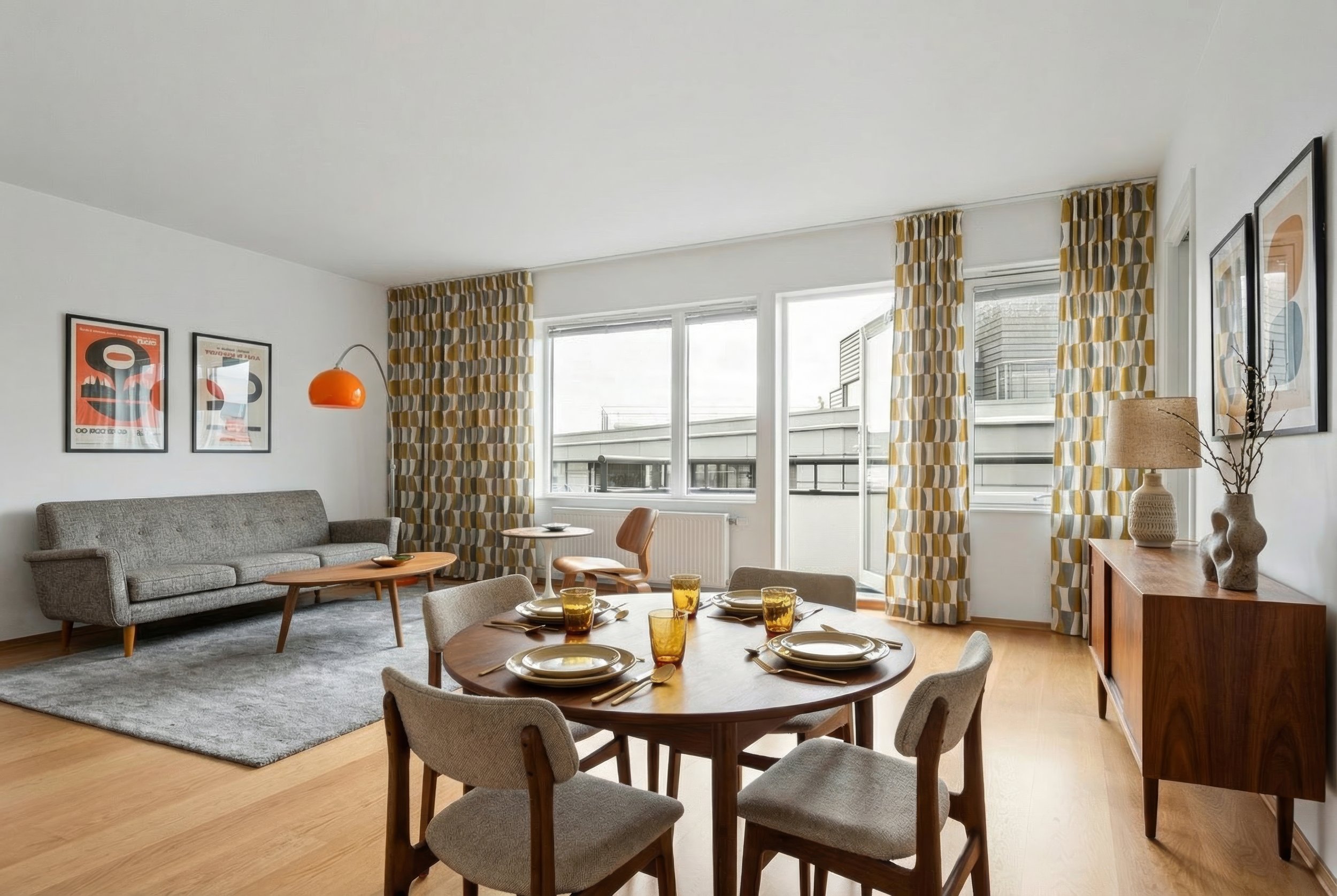 Gemütliches Wohnzimmer mit Esstisch, Sofa, Sesseln, modernen Kunstwerken und bunten Vorhängen vor großen Fenstern