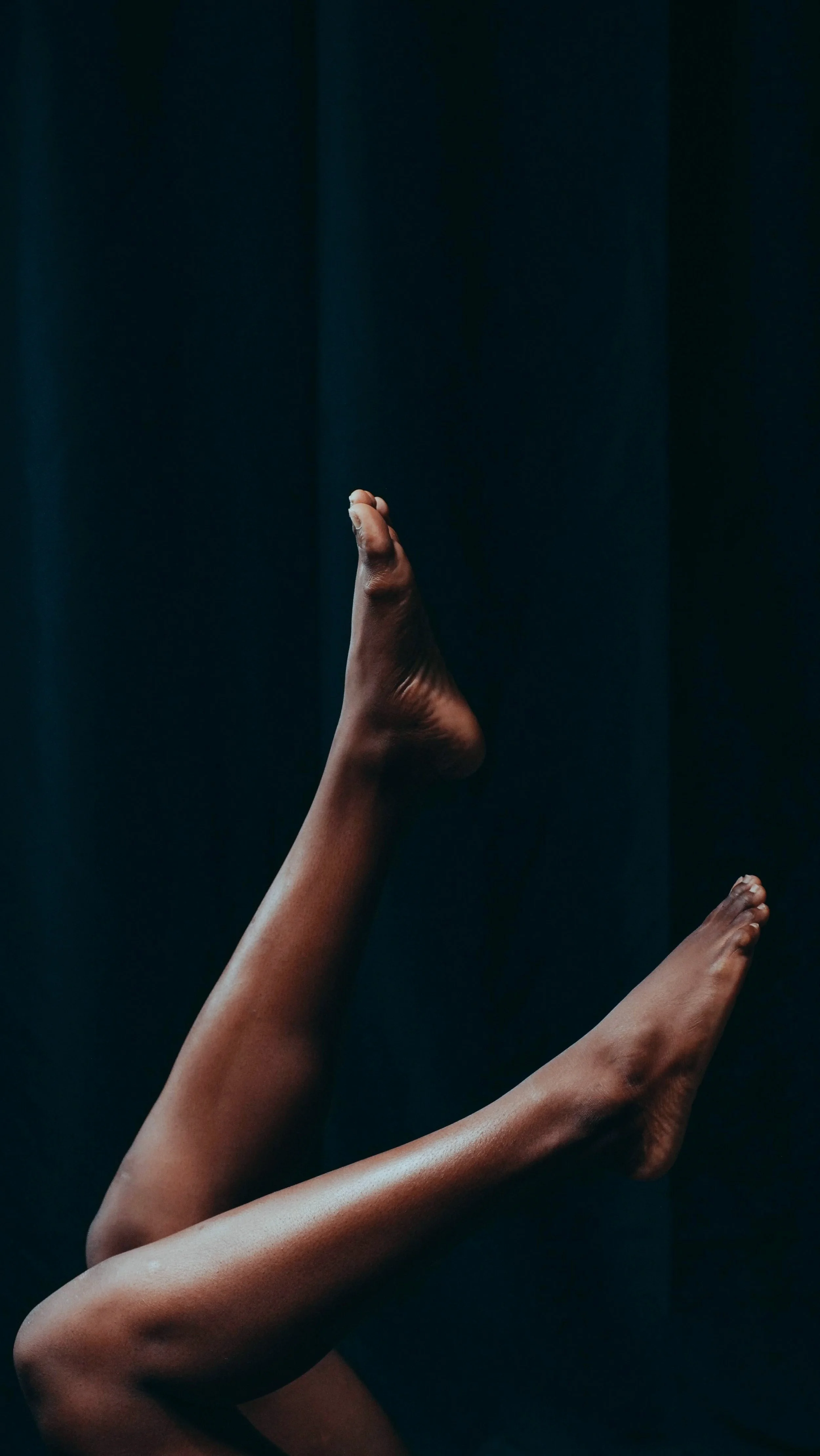 Close-up of two bare legs and feet against a dark background.