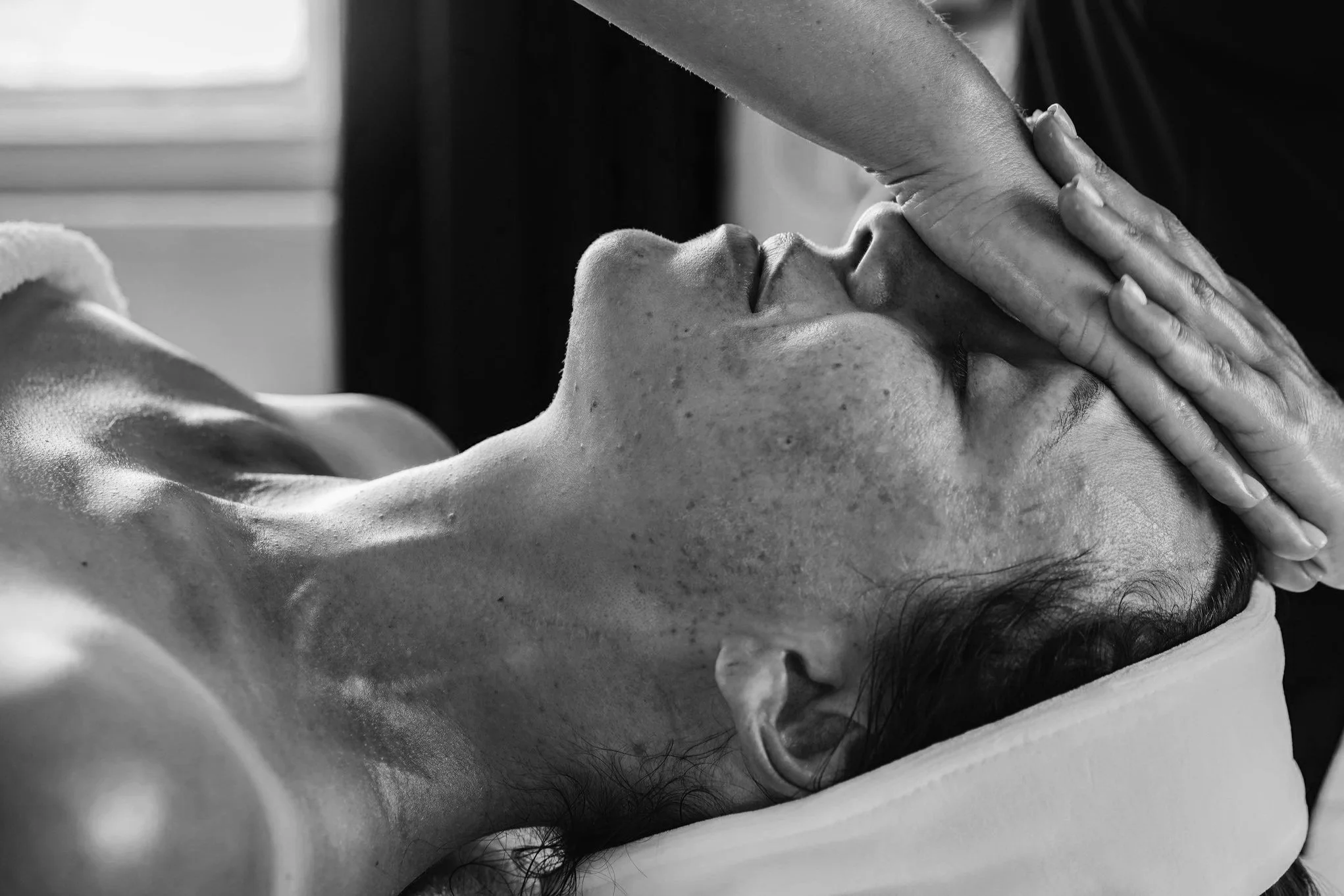 Person receiving a facial massage, hand on forehead, monochrome photo.