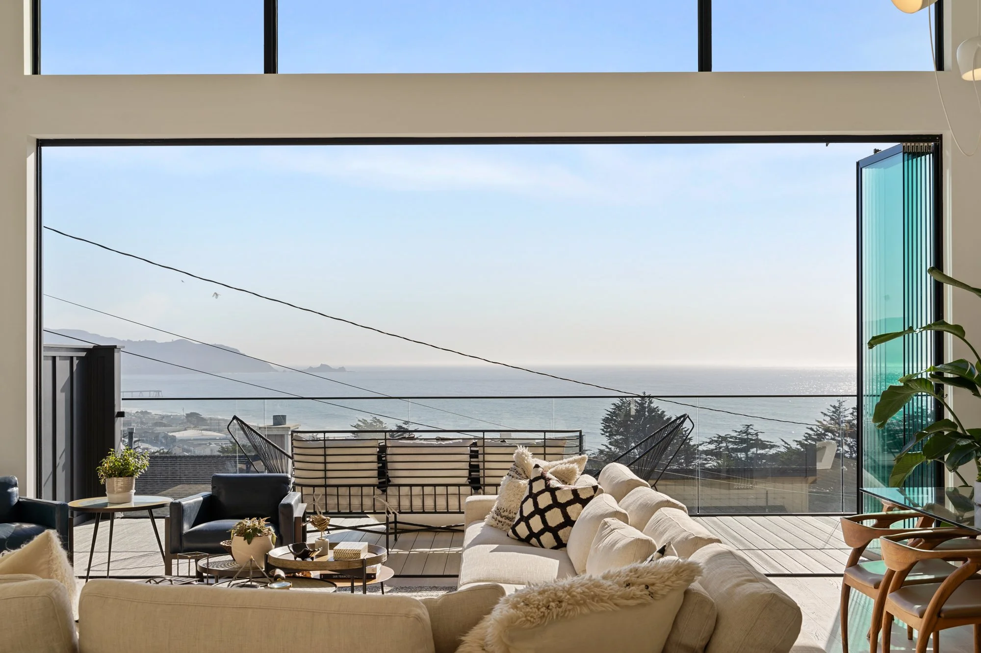 Light-filled living room opening onto a deck with ocean views, from Kitt Flood’s listing photography.