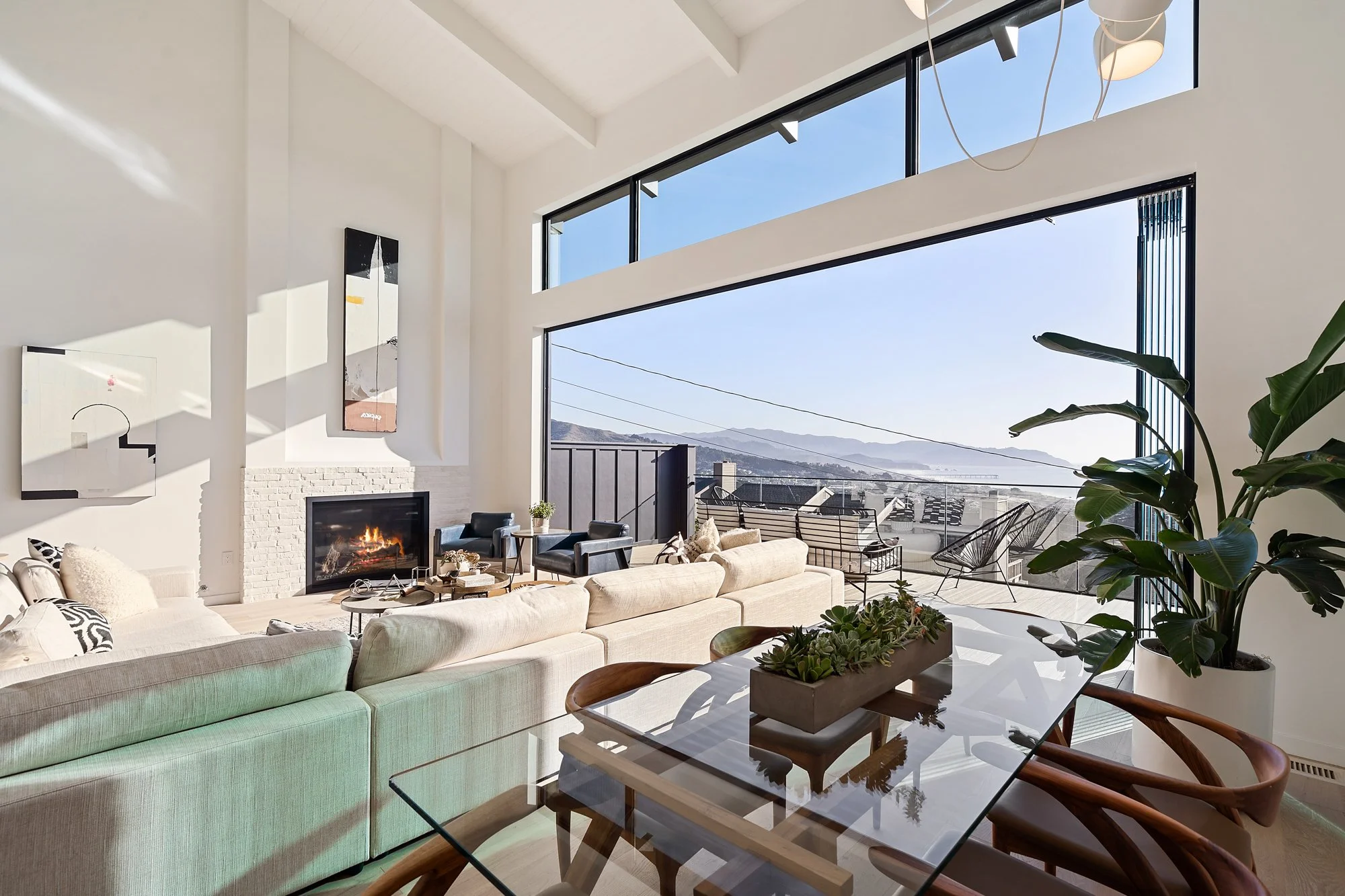 Open-plan living and dining room with fireplace, deck and ocean views, from Kitt Flood’s listing archive.