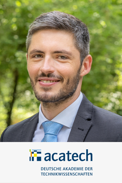 Porträt eines Mannes in einem dunklen Anzug mit blauer Krawatte, smiling, im Grünen.