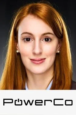Nahaufnahme von einer jungen Frau mit roten Haaren, weißem Hemd und dunklem Blazer, die freundlich in die Kamera lächelt, mit dem PowerCo-Logo unten.
