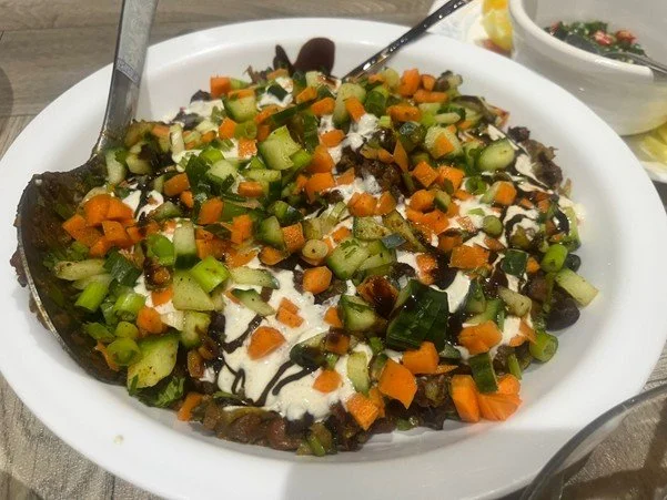 Bowl of food topped with carrots and cucumber with spoon