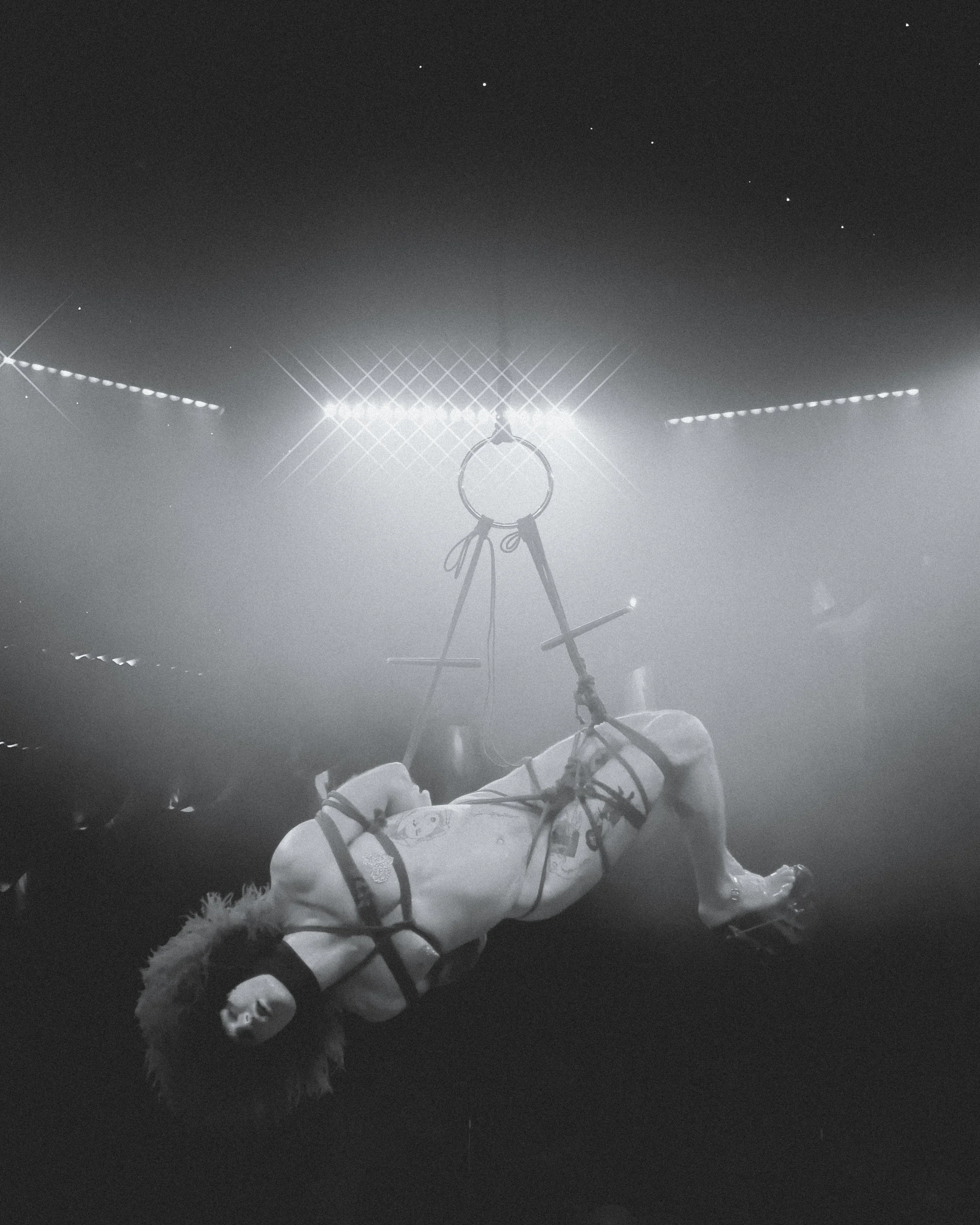 Astronaut lying on the ground during a space mission with a space suit and helmet, looking up at stars with a bright light source overhead, in black and white.