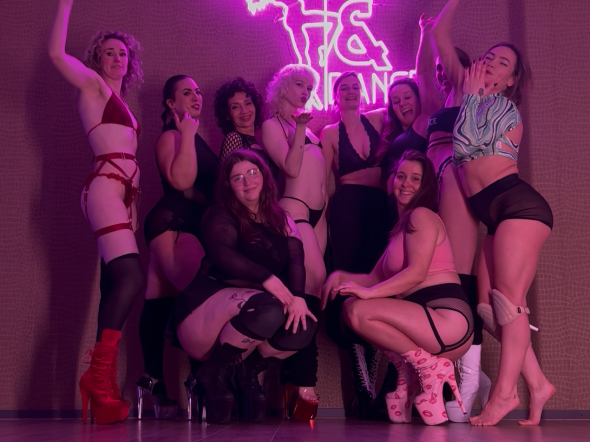 A group of women dressed in lingerie and high heels posing in front of a neon pink sign that says 