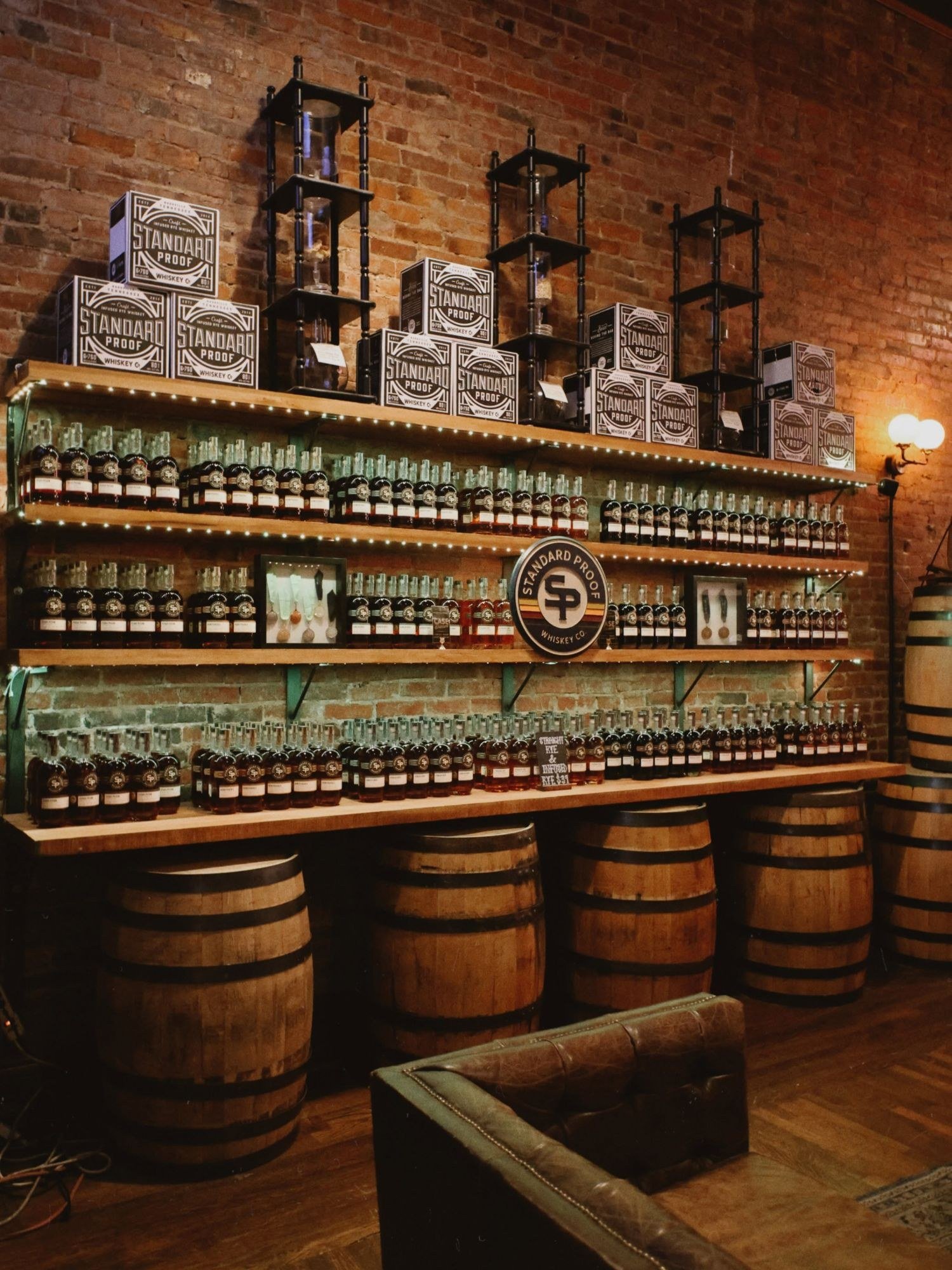 The Standard Proof bottle wall: shelves of whiskey over barrels against exposed brick in the Nashville tasting room