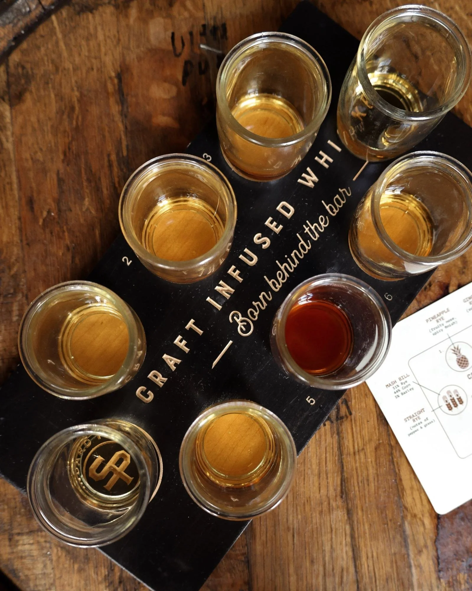 A flight of eight Standard Proof whiskeys on a board reading Craft Infused Whiskey, Born Behind the Bar