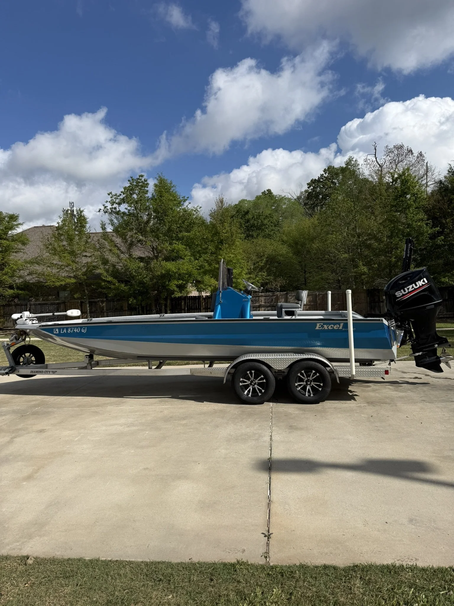 A small Tracker boat on a trailer parked near a body of water with hills and trees in the background and a partly cloudy sky.