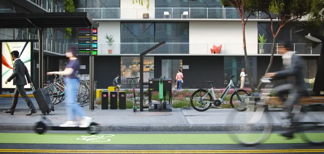 cyclist and person on scooter ride on a bike lane past a bike parking area at a transit stop. A scooter is parked as well as an e-bike.