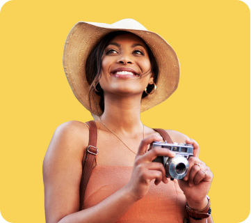Smiling woman wearing a hat and holding a camera against a yellow background.
