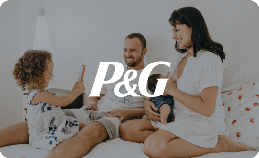 Family of three sitting on bed, parents and young daughter, smiling, using a tablet, with P&G logo overlay.