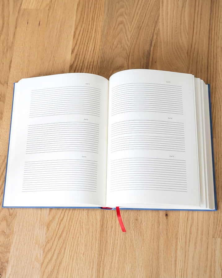 Open blank planner or diary with lined pages for writing, sitting on a wooden table with a red ribbon bookmark hanging from the bottom.