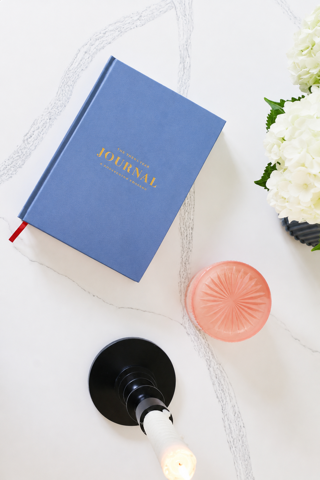 Blue journal styled with flowers/candle:
    PRCHMNT three-year reflection journal styled on a marble table