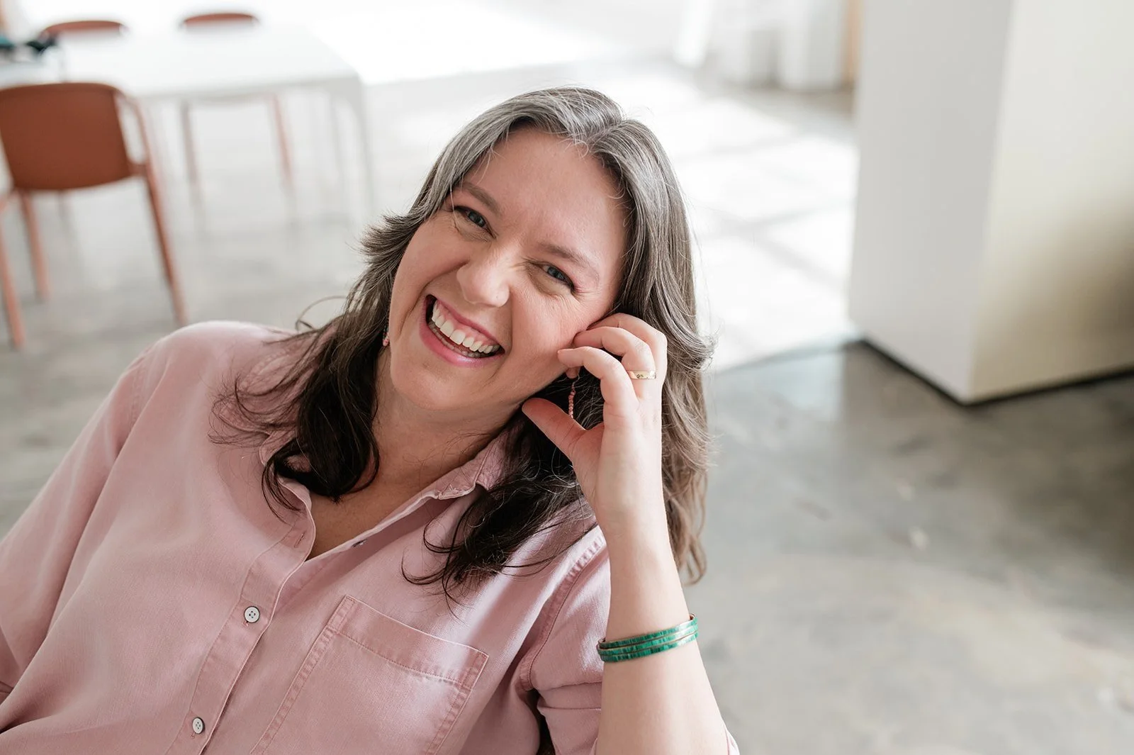 Woman smiling in a bright room wearing a pink shirt and a turquoise bracelet.