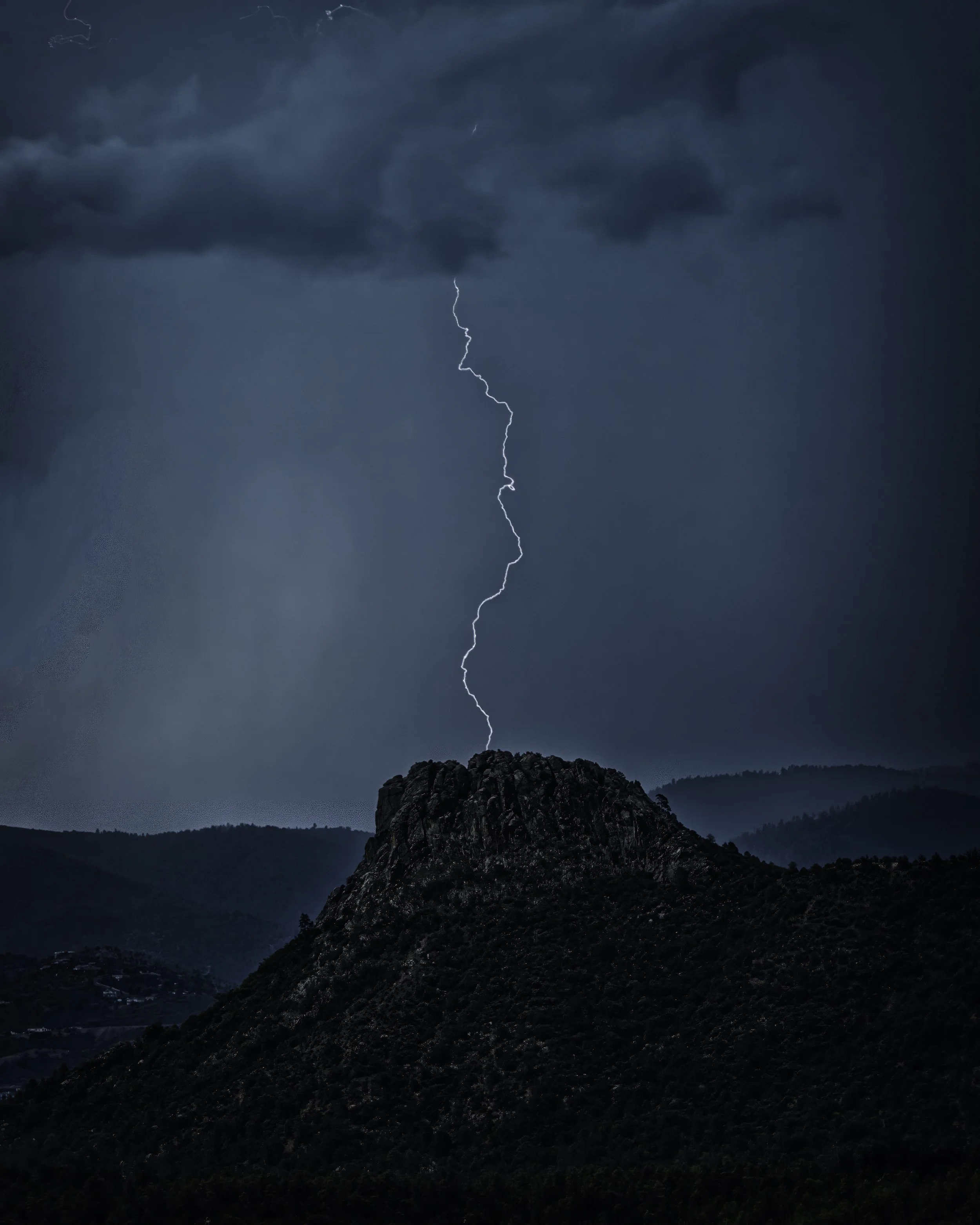 FIRST STRIKE – Pounded by hail and wind, I weathered the elements while perched atop a mountain ridge to capture this singular bolt of lightning over Thumb Butte in Prescott, Arizona.