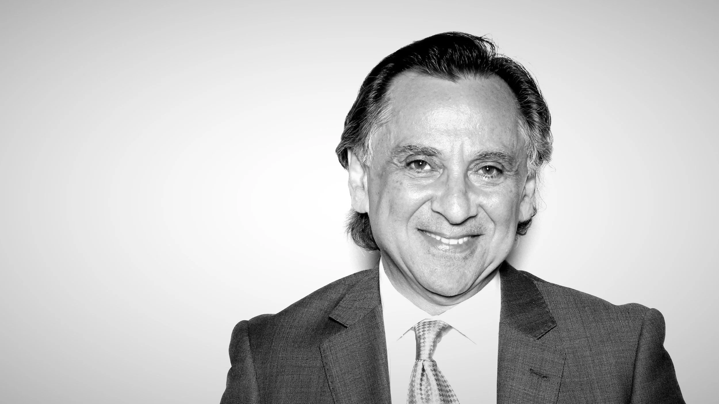 Black and white portrait of a man with dark hair, dressed in a suit, smiling.
