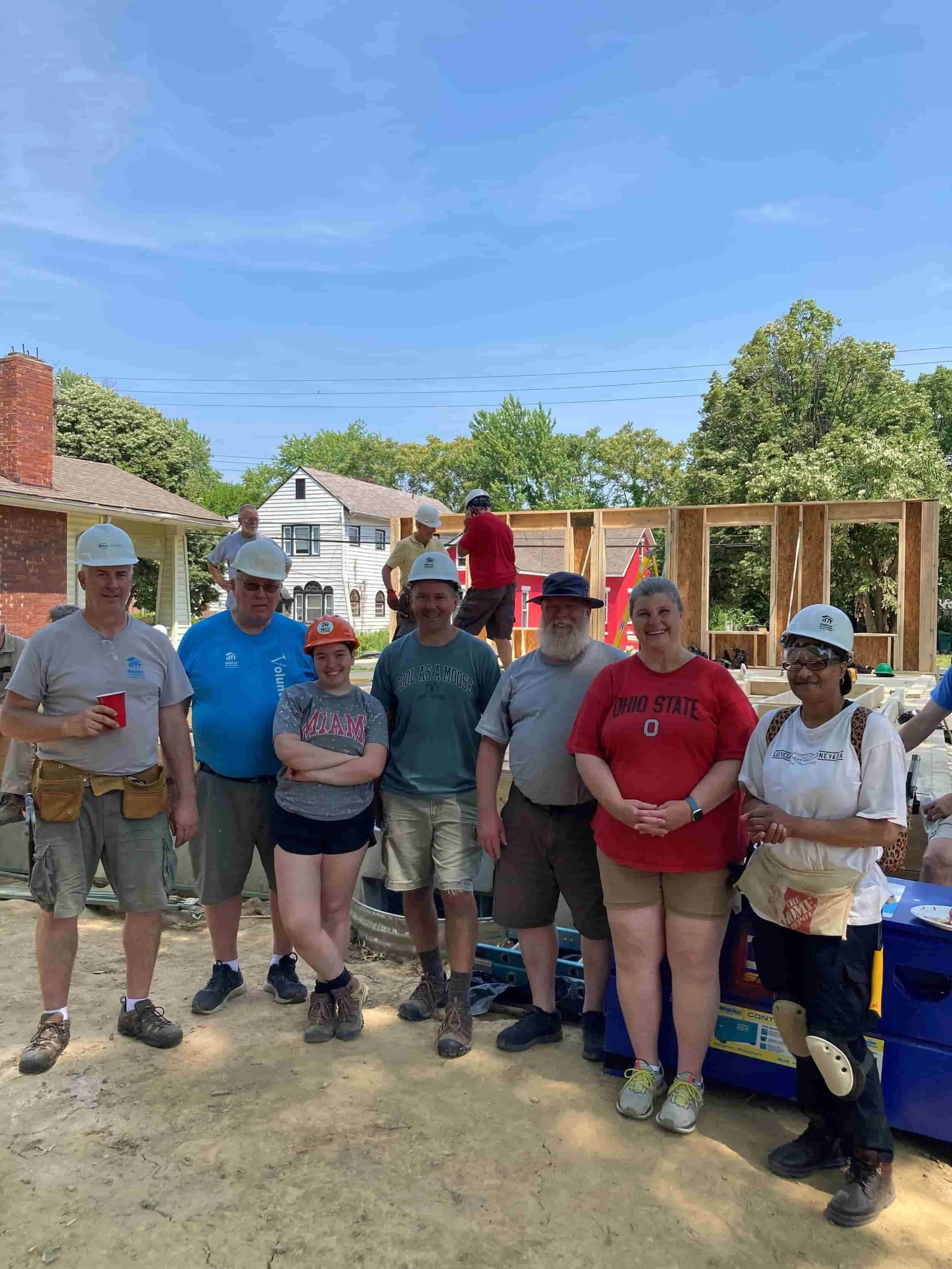 Volunteers with hard hats gathered for a picture in front of a home build site for Habitat for Humanity.