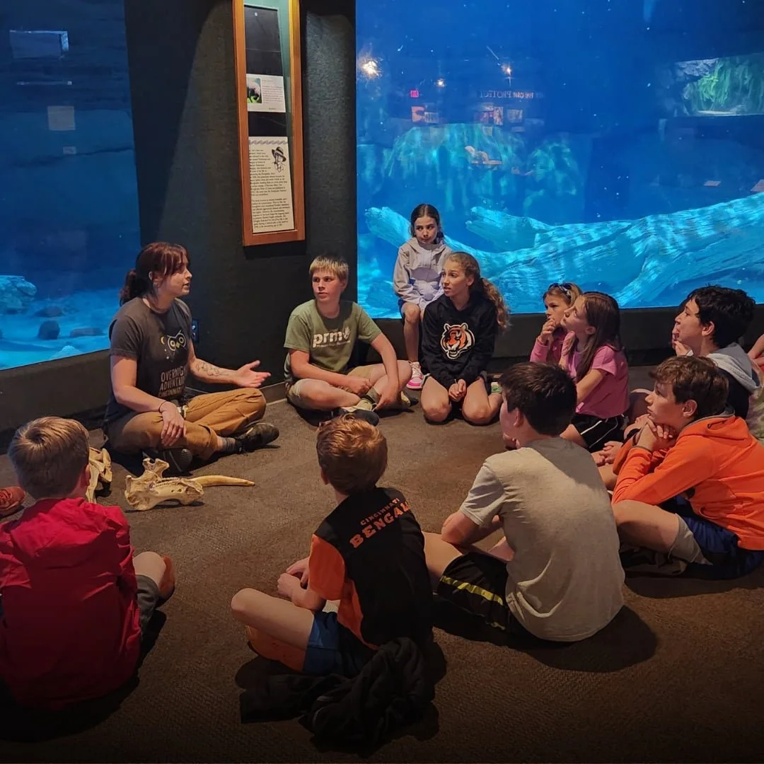 Students gathered around a circle in a room with an aquarium during a retreat at the zoo.