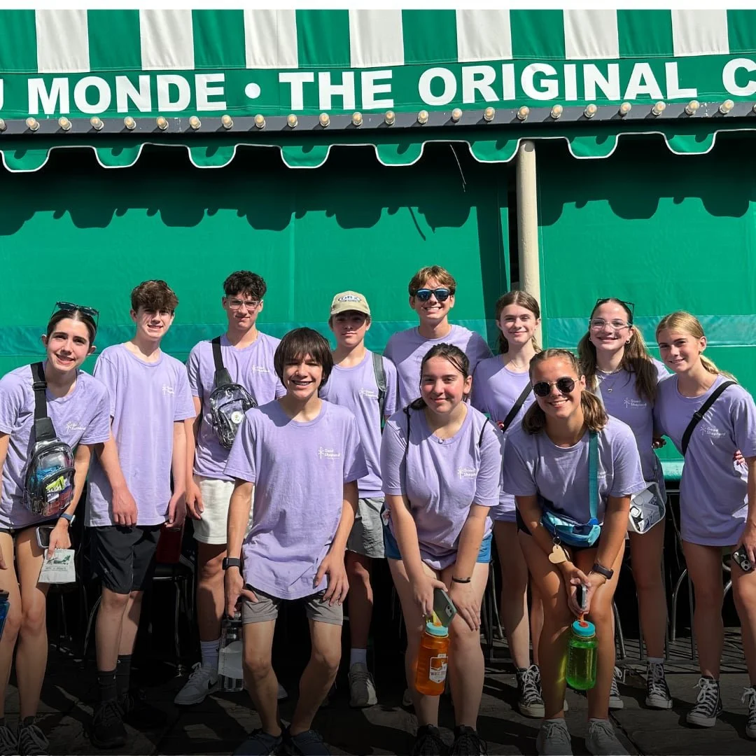 Group of teenagers wearing matching light purple t-shirts standing in front of restaurant.