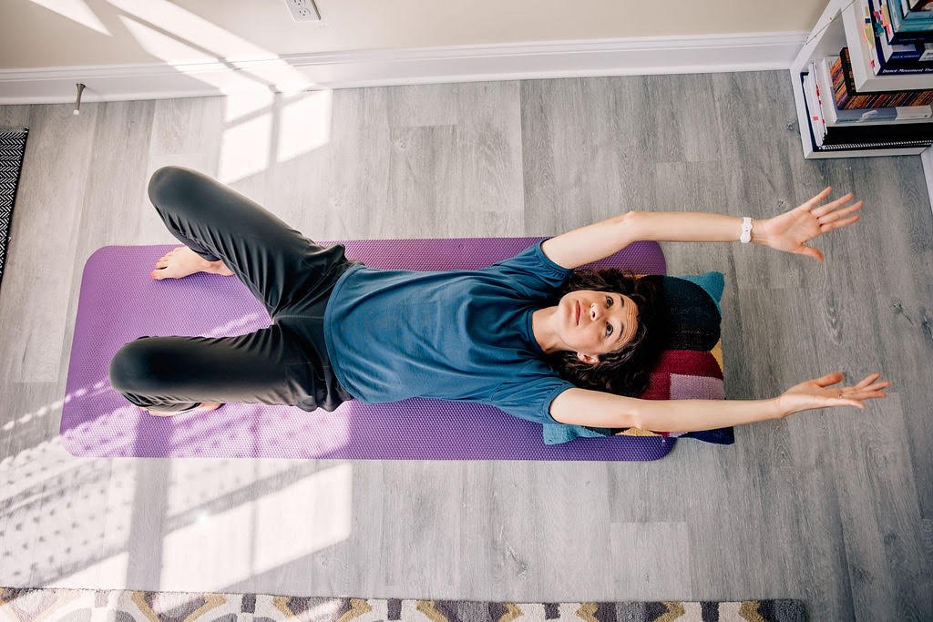 Kim lying with her back on the floor reaching her hands vertically.