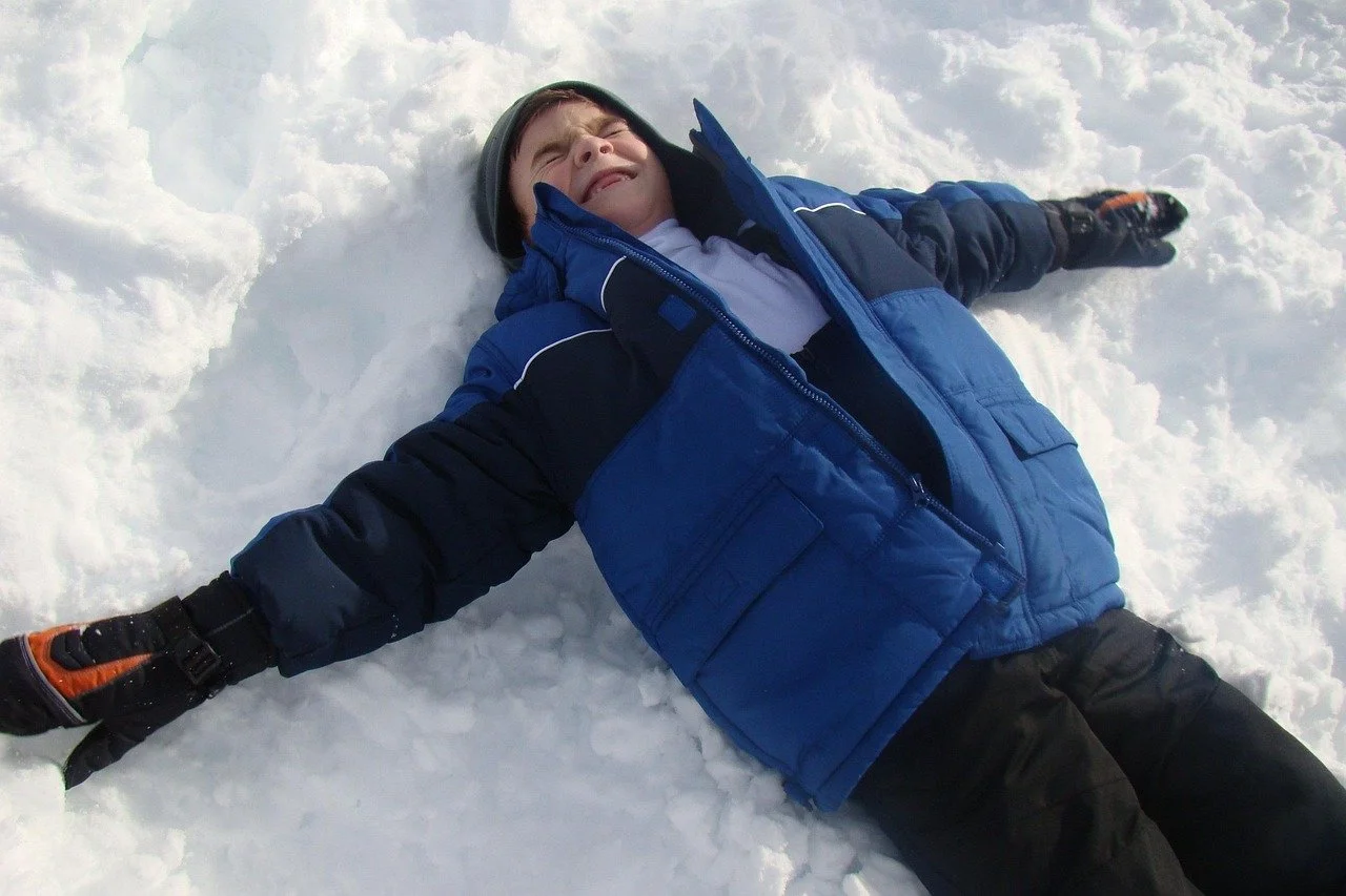 Child wearing a coat making a snow angel.