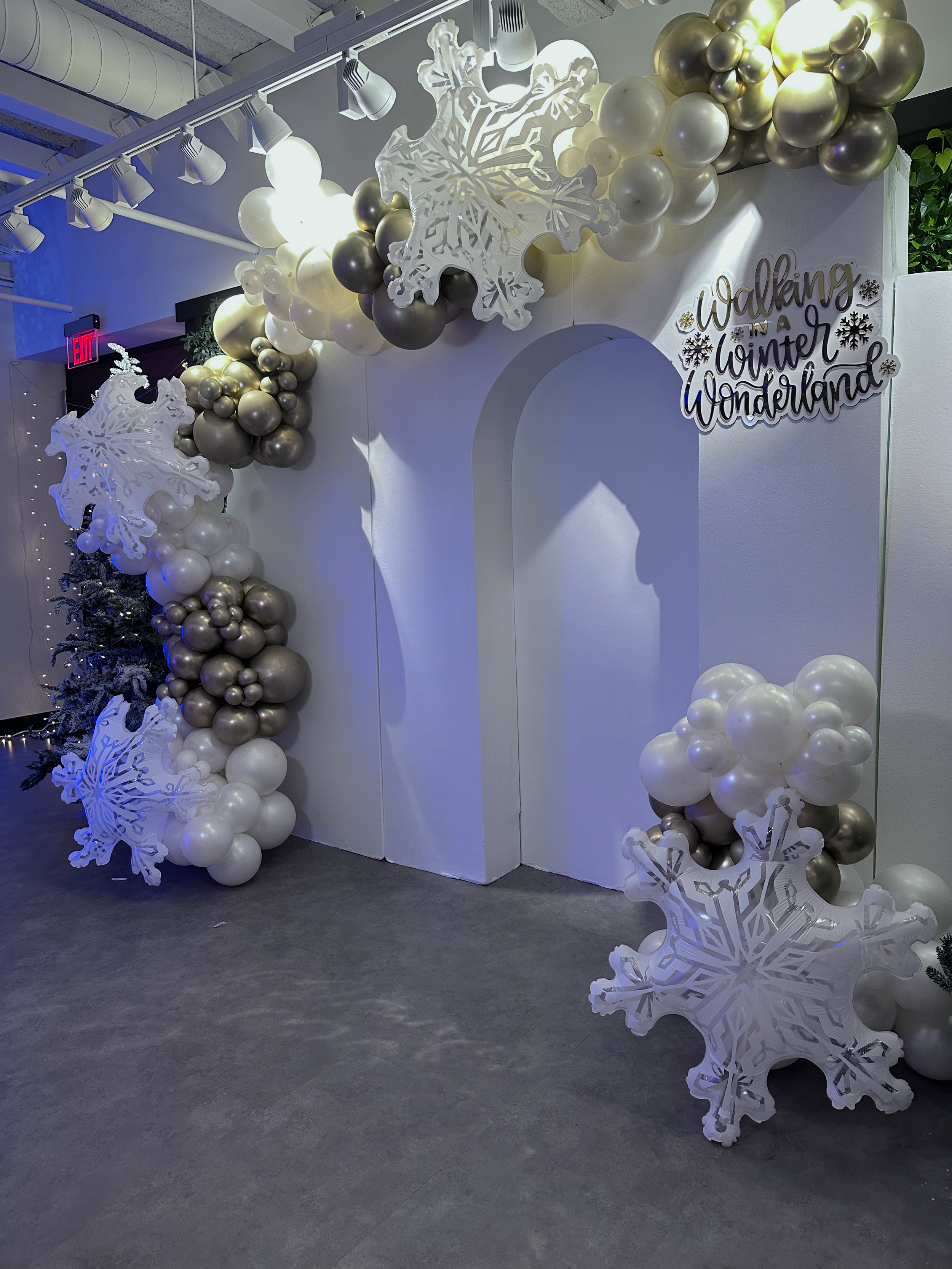 Decorative winter-themed setup with white, gold, and silver balloons, illuminated snowflake cutouts, and a sign that reads 'Walking in a Winter Wonderland'.