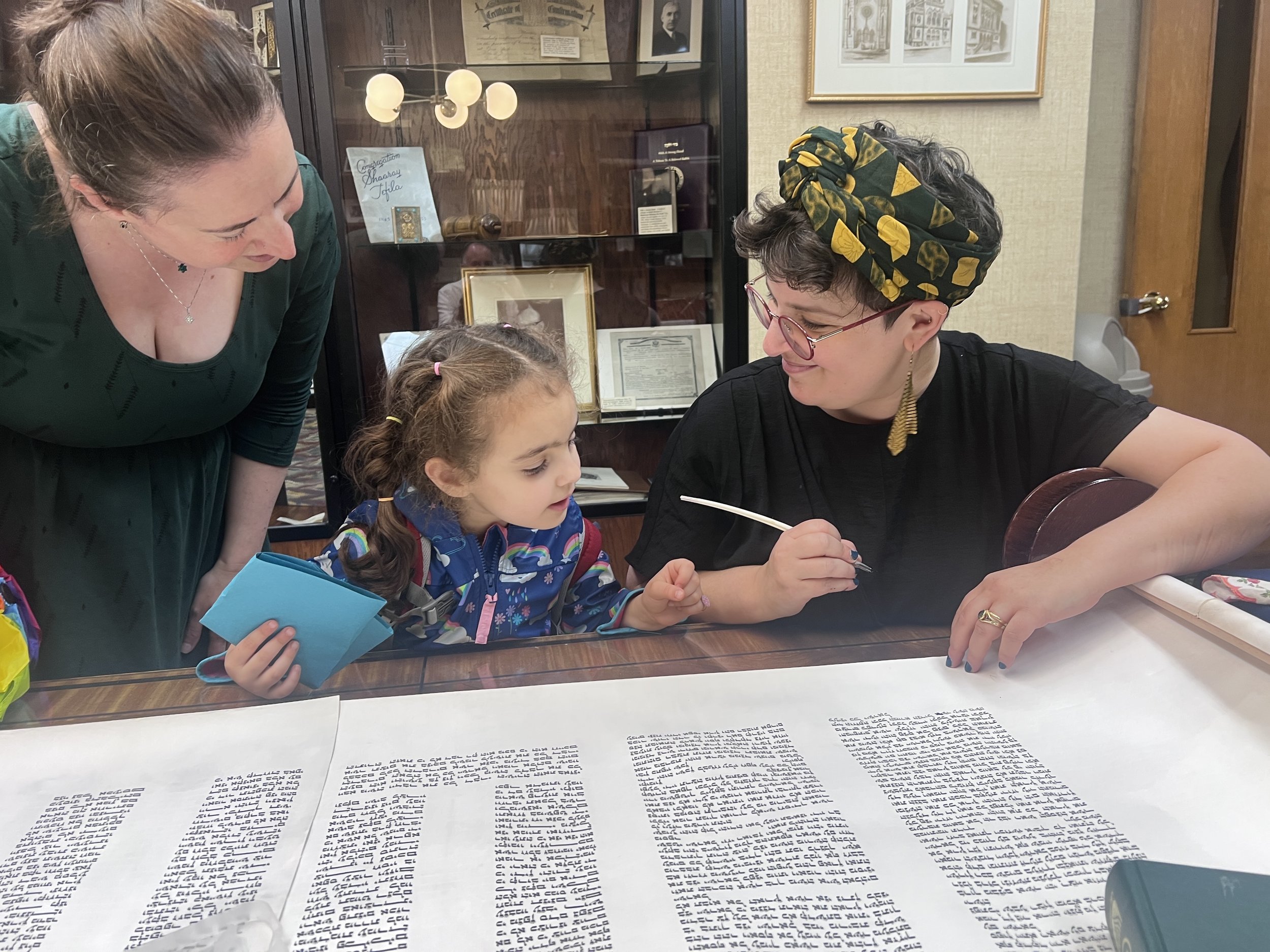 a young assistant helps fill in letters in a sefer torah