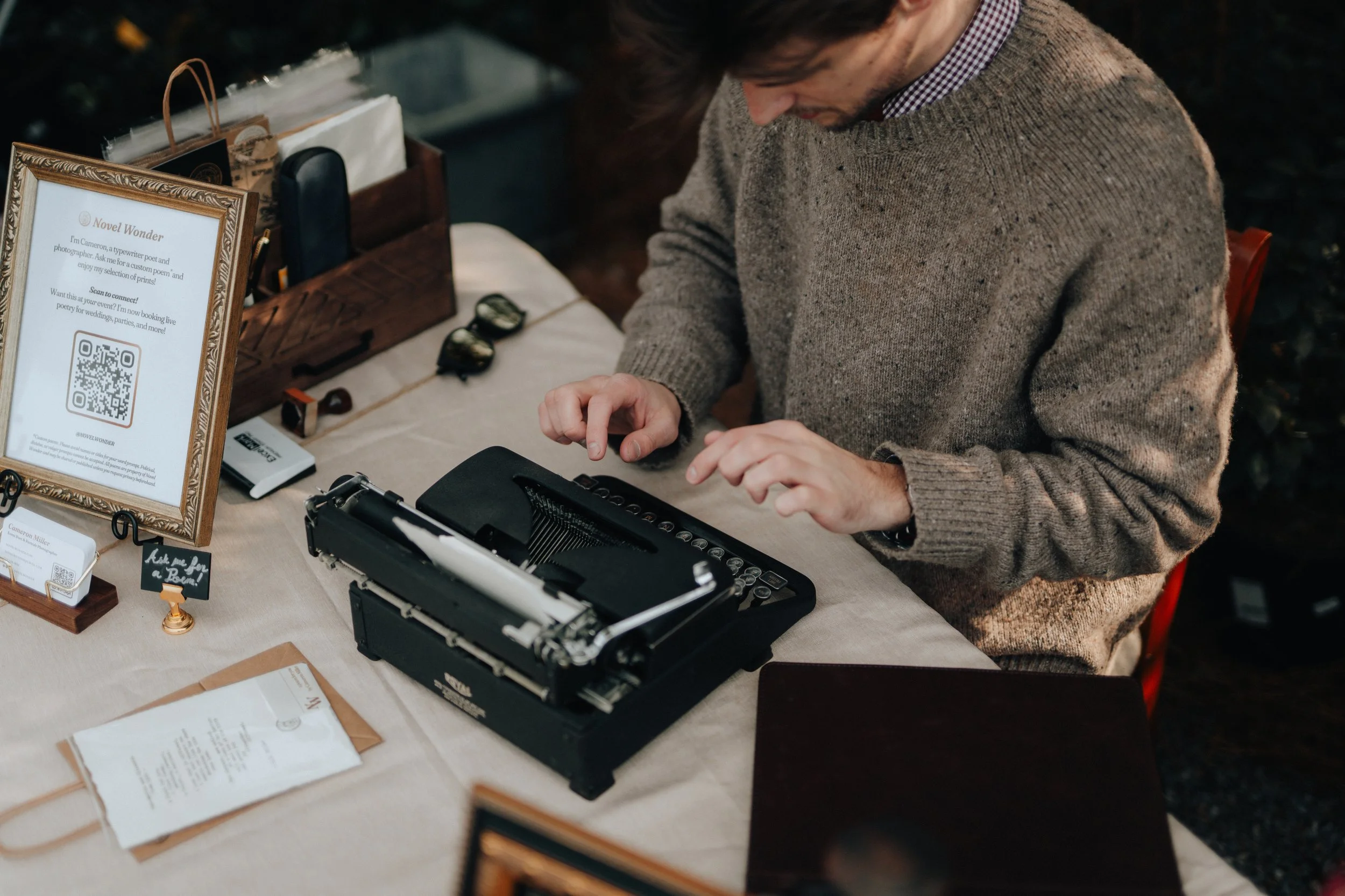 A man using a vintage typewriter to make a poetry at a table decorated with framed signs.