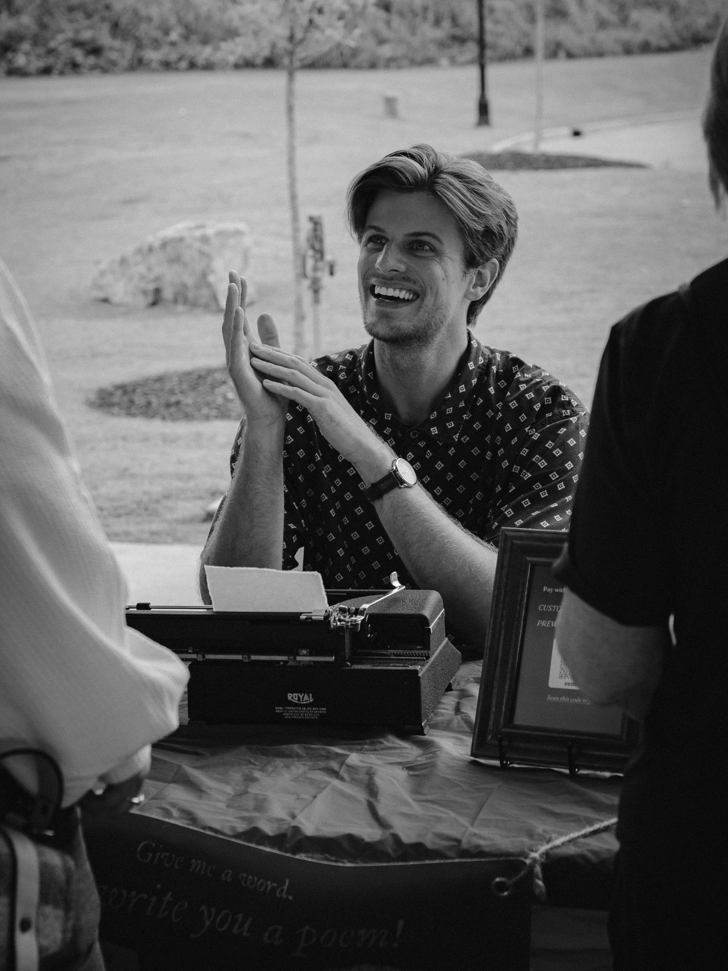 Black and white image of Cameron Miller, typewriter poet for hire, interacting with strangers at the Evans Market in Evans, GA.