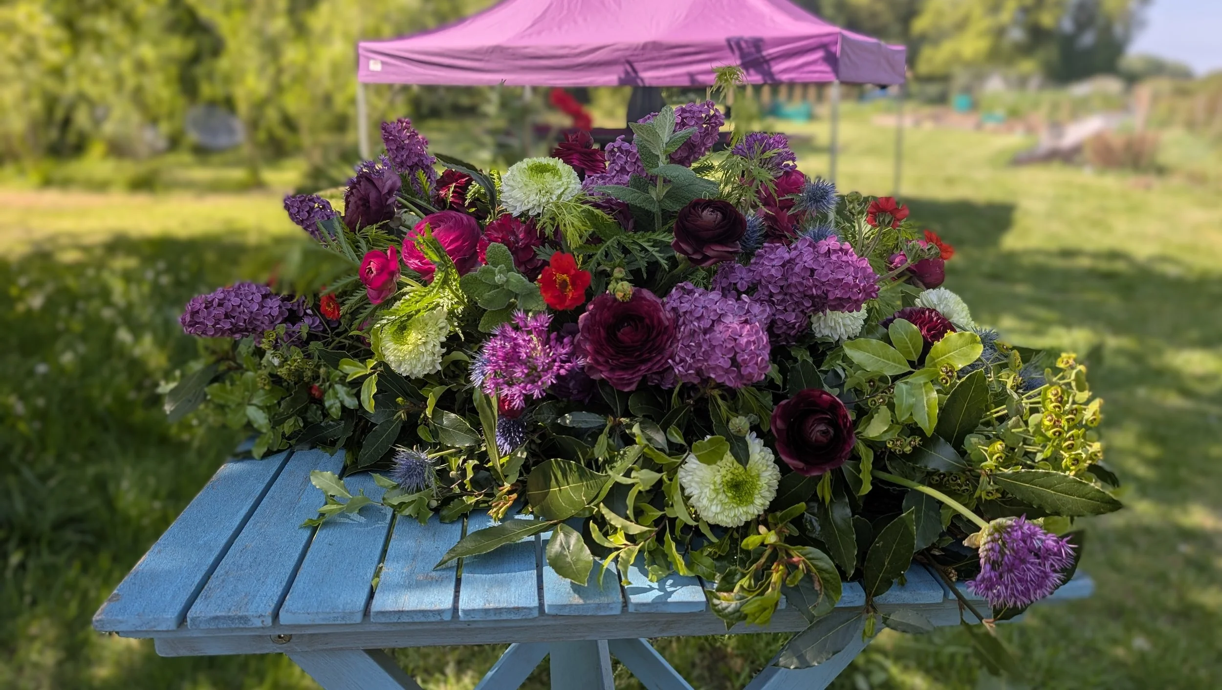 A photo of a floral farewell tribute display made up of reds, pink and white flowers and dark green foiliage