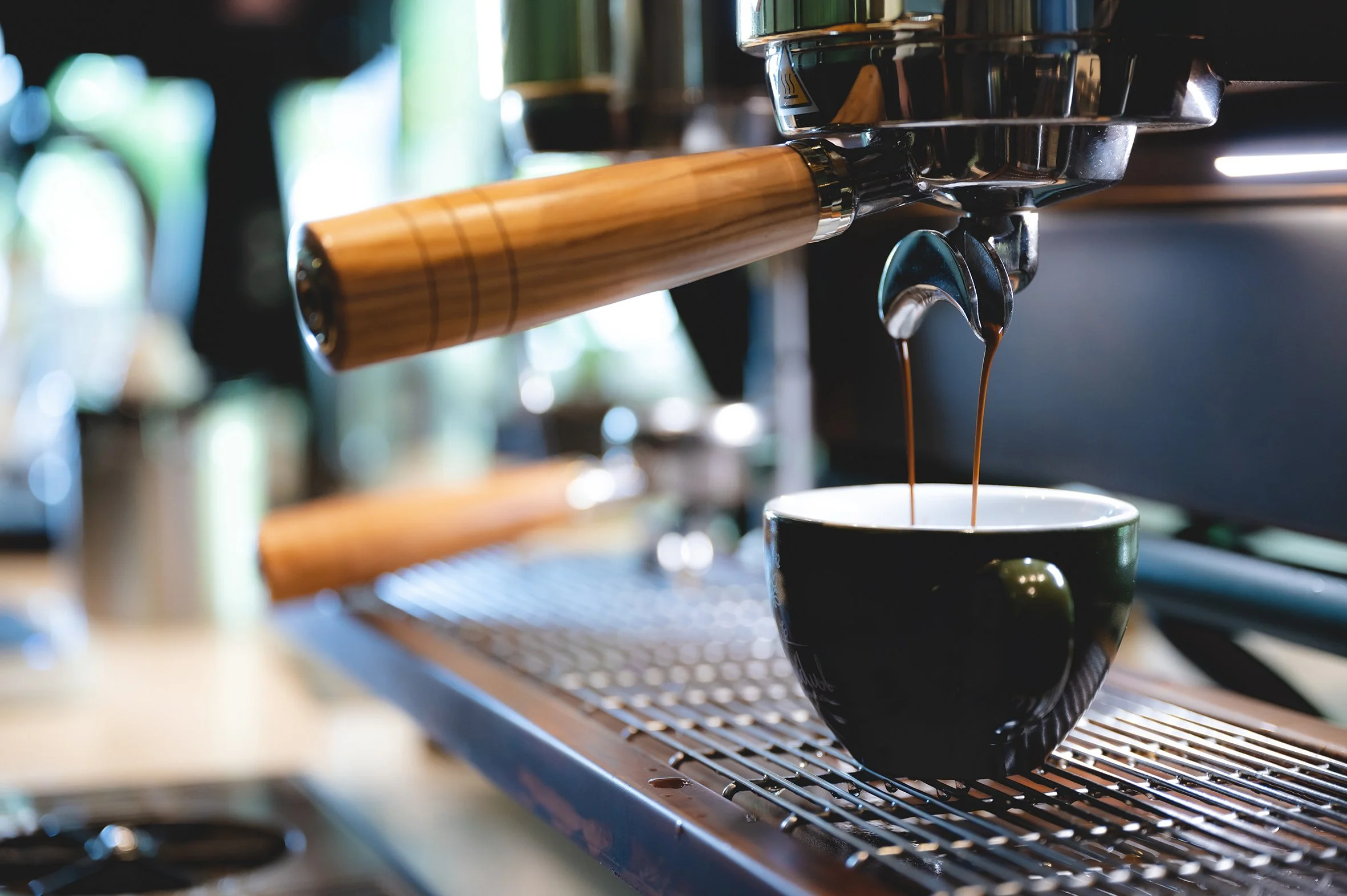 A close up of a cafe coffee machine pouring coffee into a dark green cup