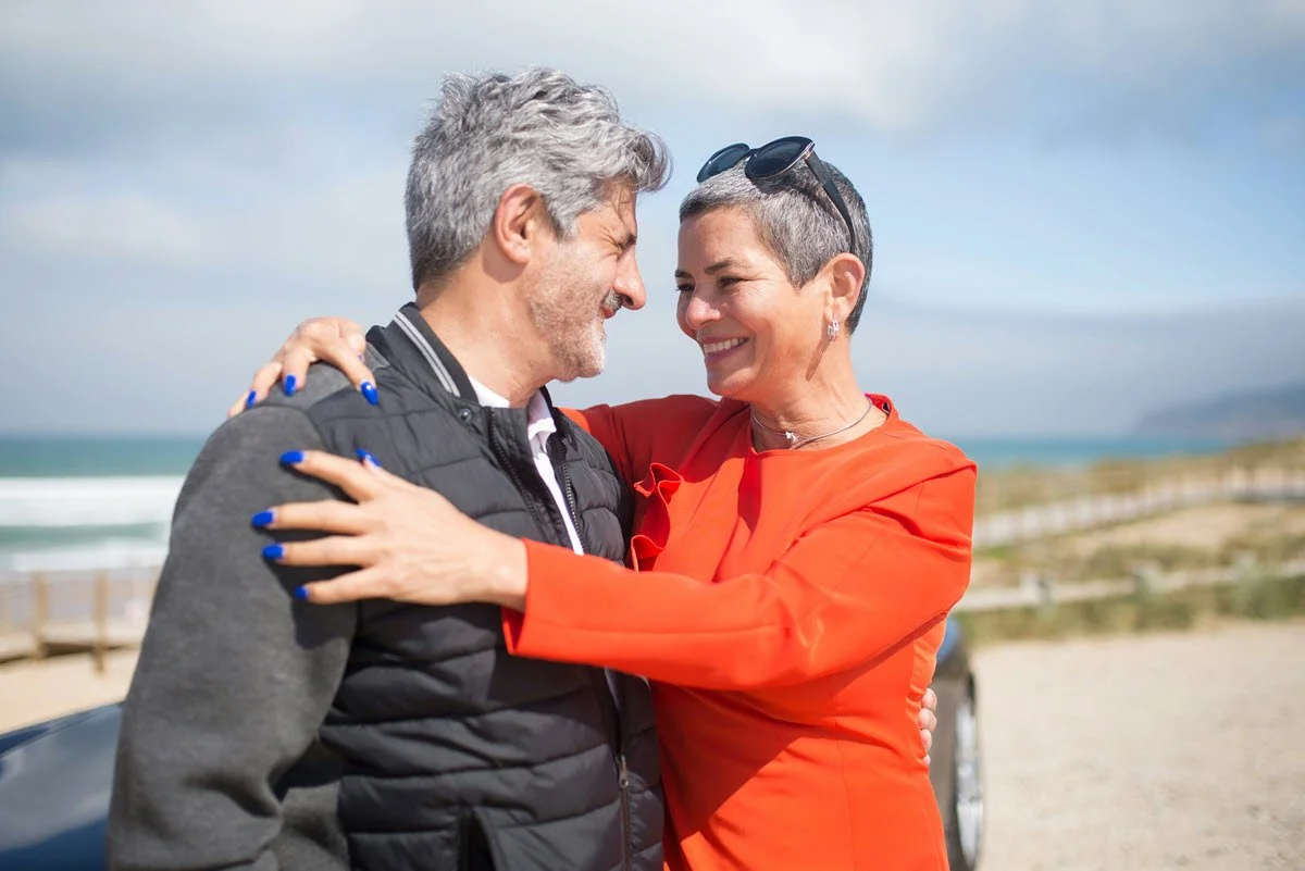 a retired couple hugging while standing by their car at the beach
