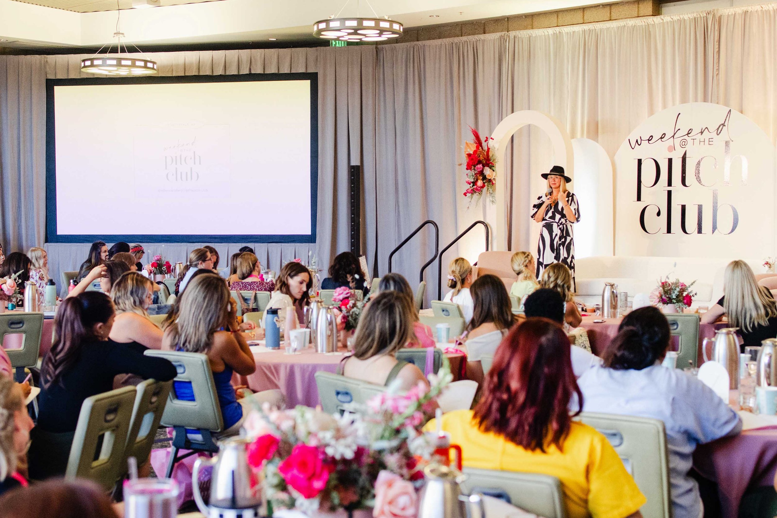 A woman speaks on a stage during a live event, footage used in a speaker reel.