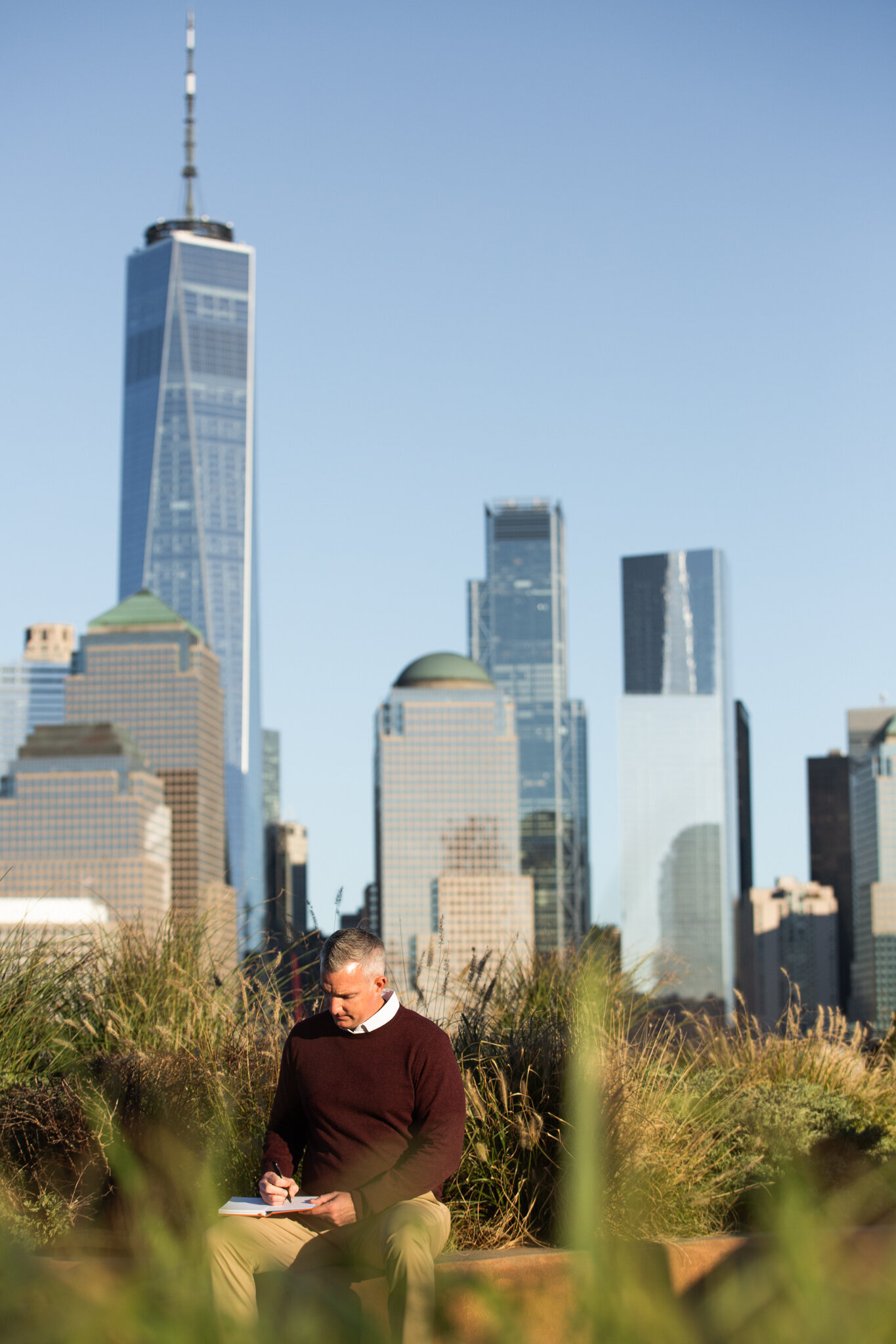 A man writes in a notebook with the NYC skyline behind him in this New Jersey brand photography session.