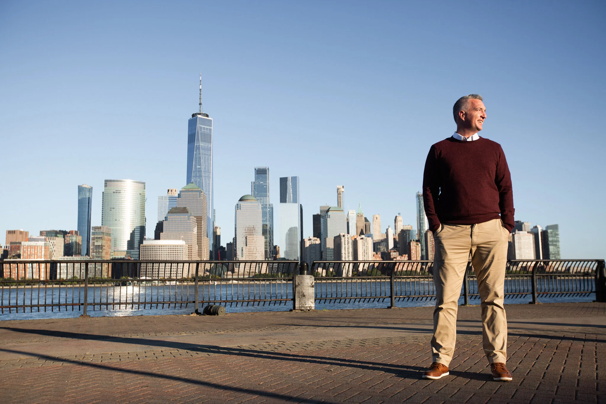 Man standing near Hudson River Waterfront Walkway with NYC skyline in the background during Liberty State Park brand photography session